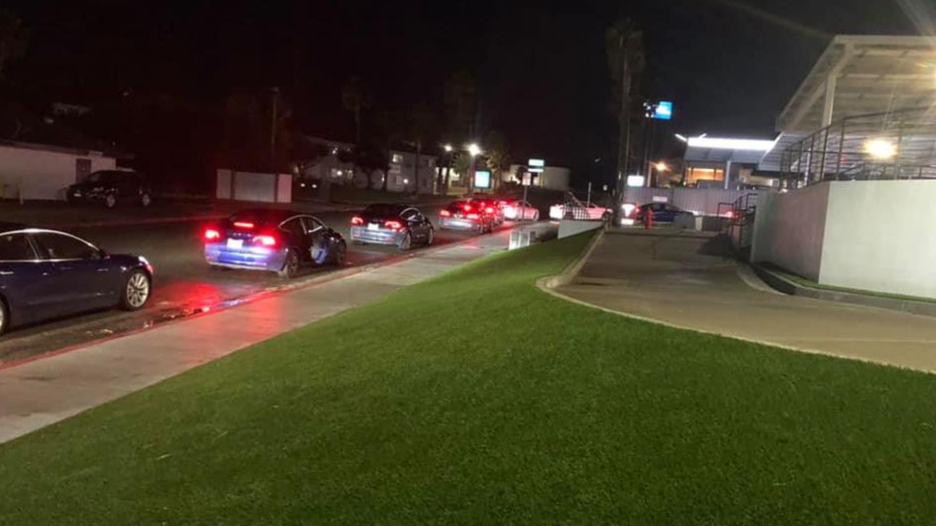 Tesla vehicles lined up waiting for Supercharger stalls at night