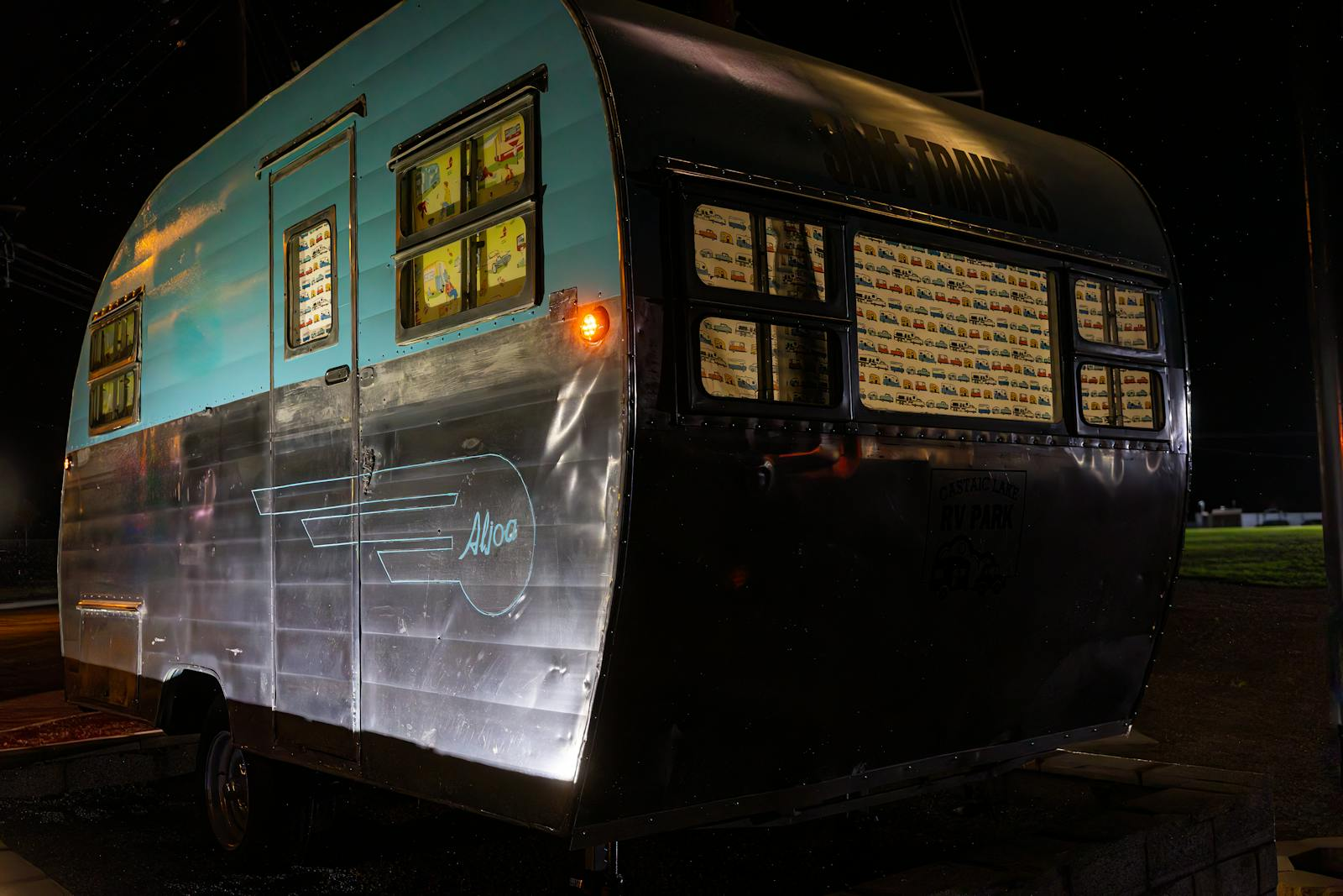 A vintage aqua and silver aluminum travel trailer parked at night, showcasing retro design.