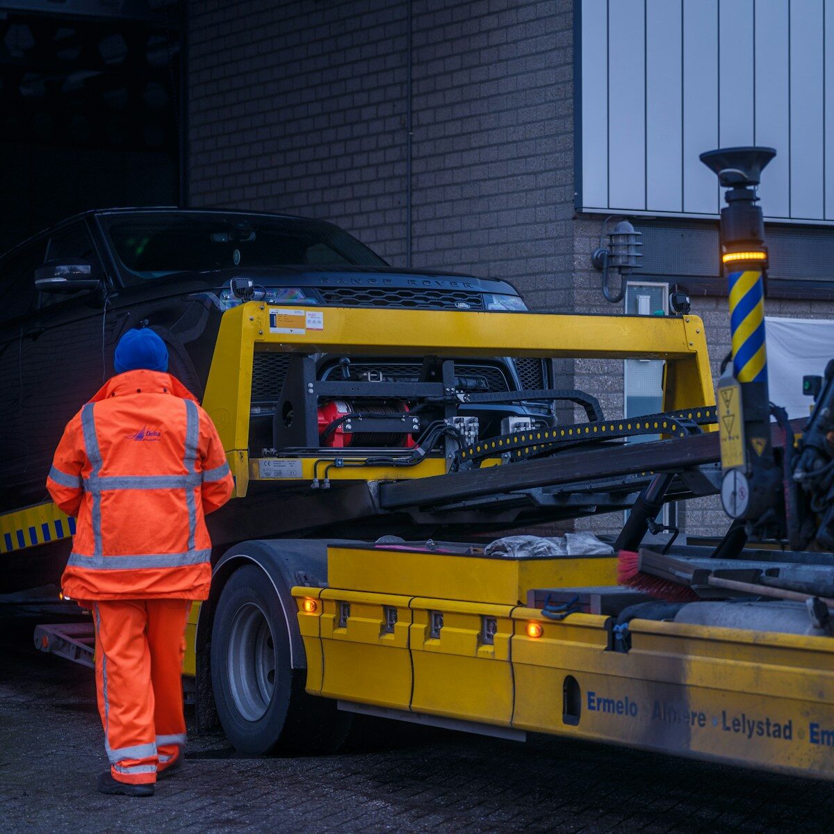 A man in an orange jacket is walking towards a truck