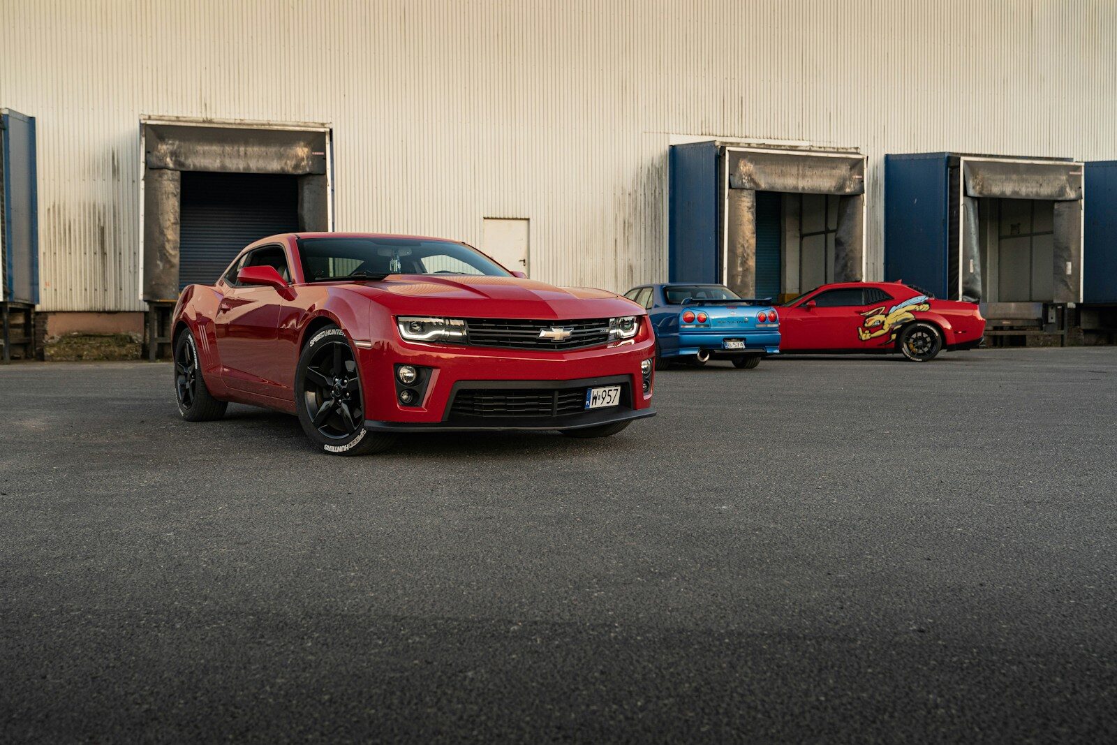 A red camaro is parked with two others.