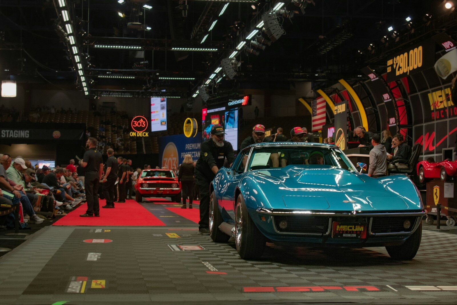 A teal classic car drives across an auction stage.