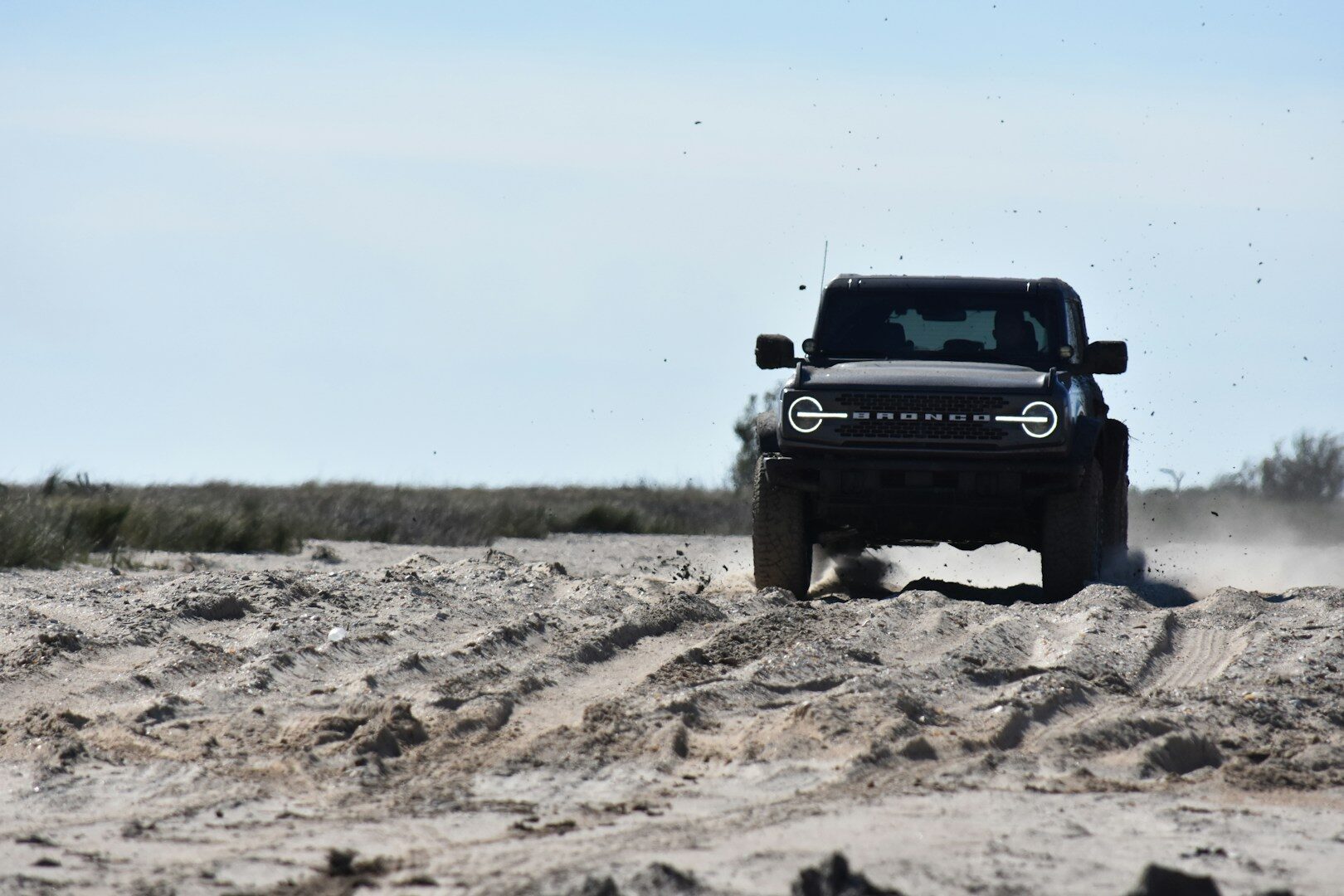 a jeep driving through the sand on a sunny day