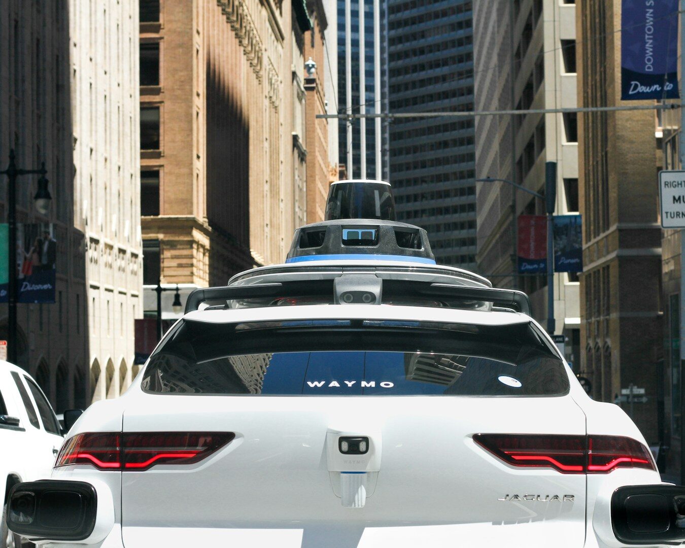 A Waymo robotaxi with visible sensor equipment drives through a city street