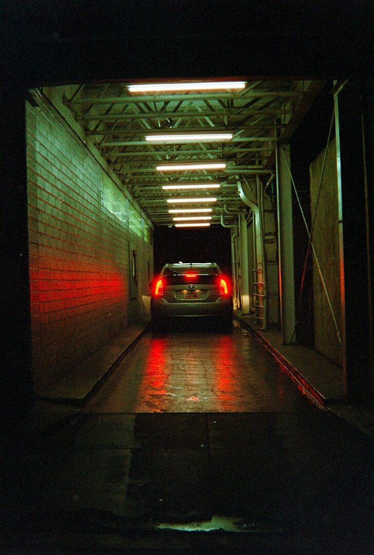 Car driving through a dark tunnel with red taillights.