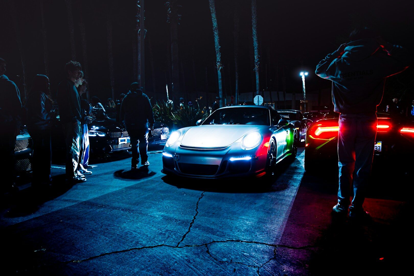 Cars and people gather on a dark street.