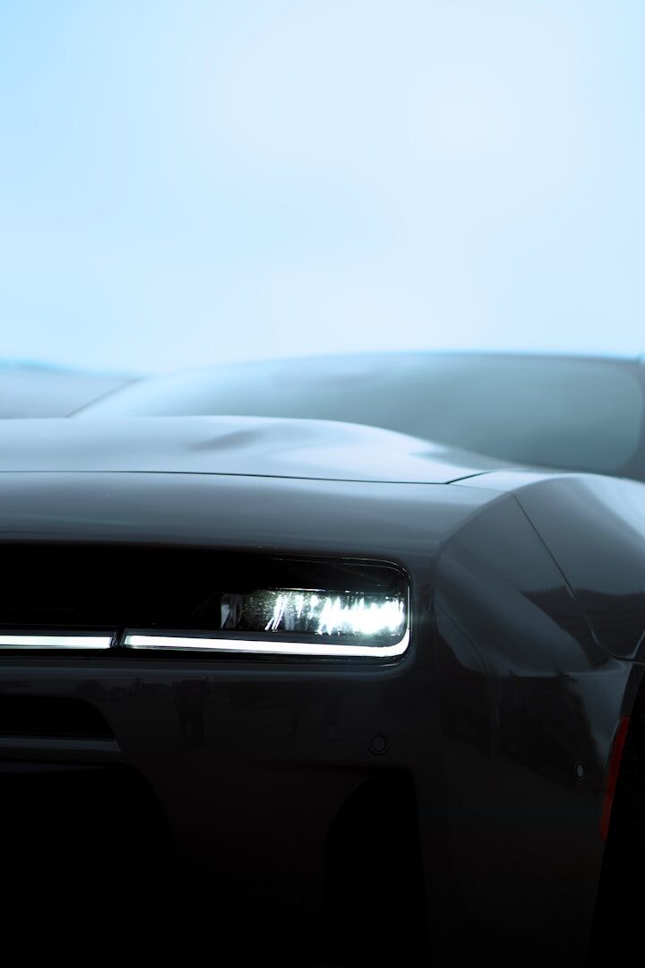 Sleek dark car with a bright, illuminated headlight
