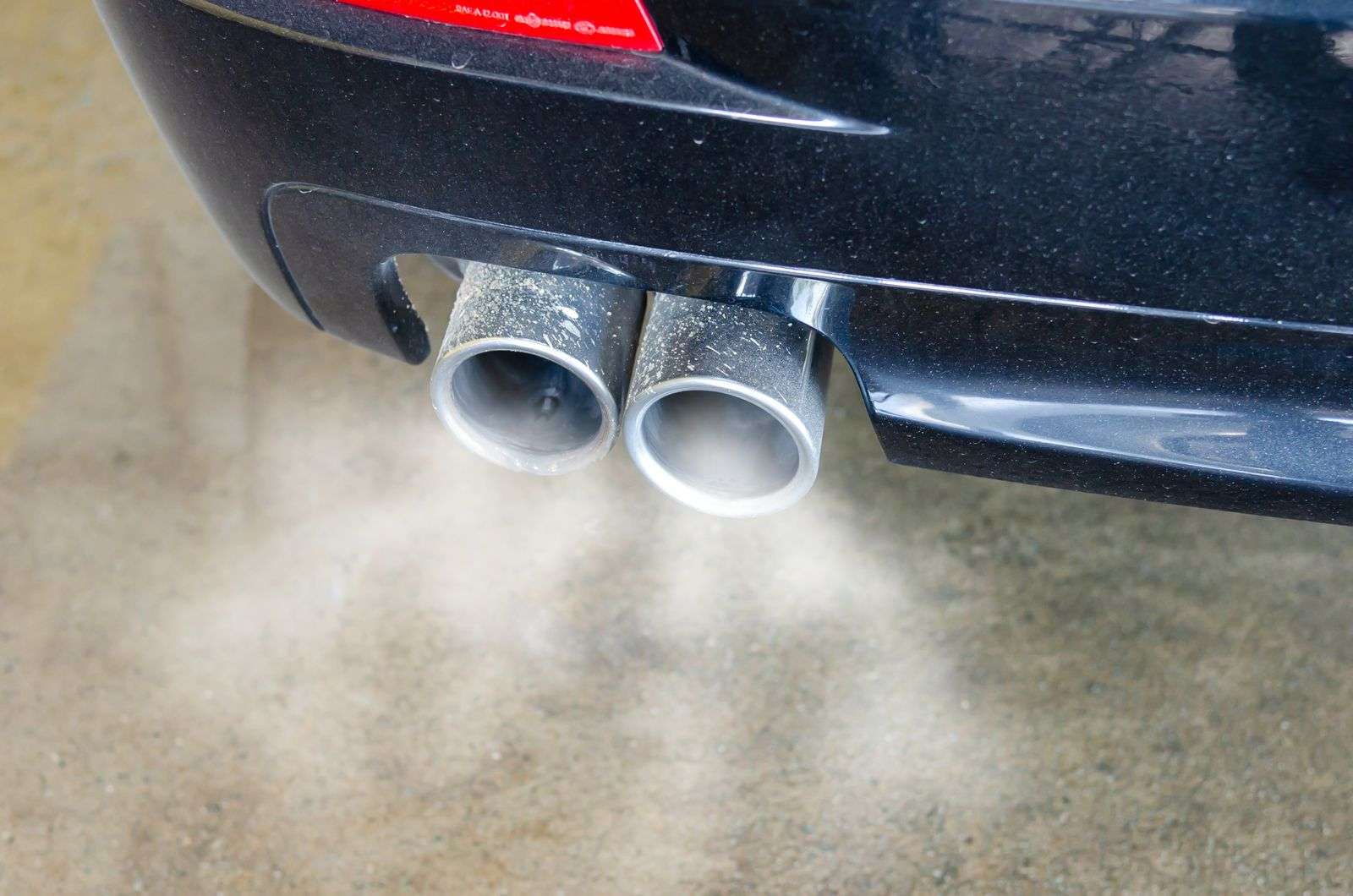 Close-up of a car's dual exhaust pipes releasing visible smoke