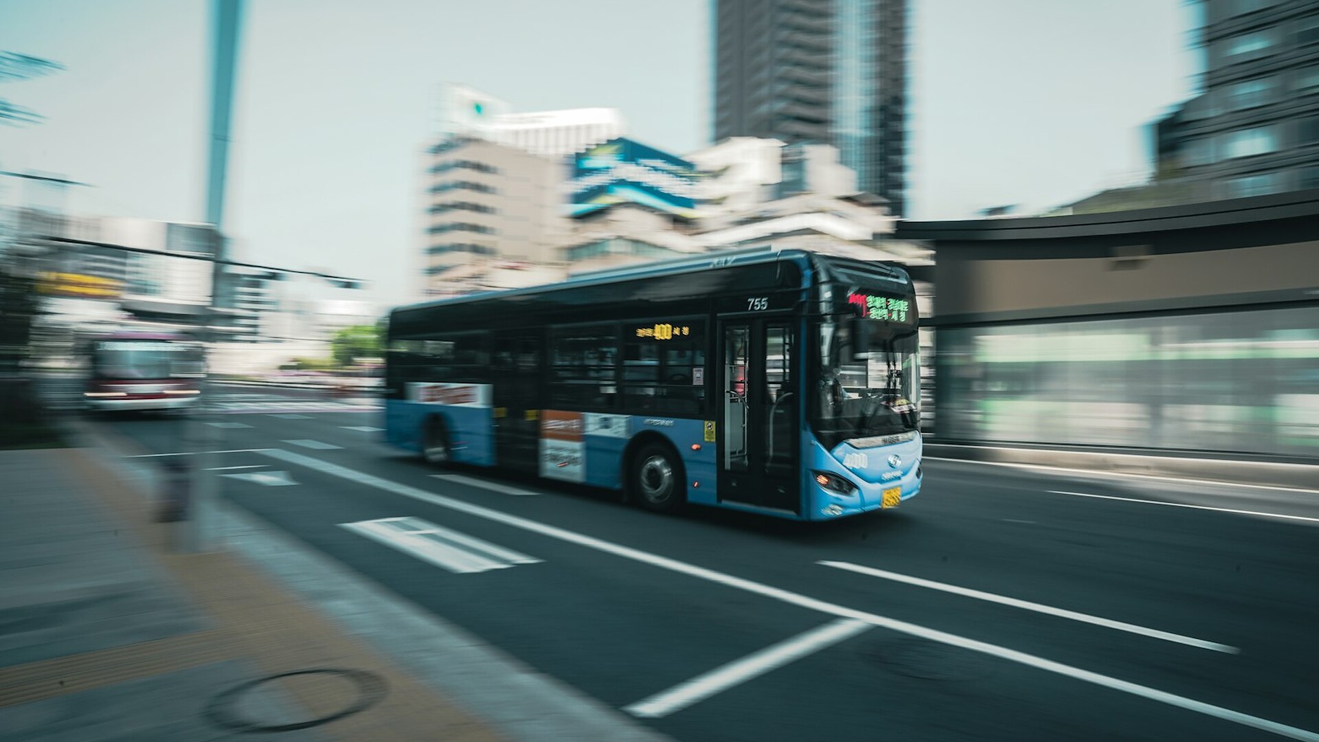 A blue electric city bus blurs past tall buildings on an urban street