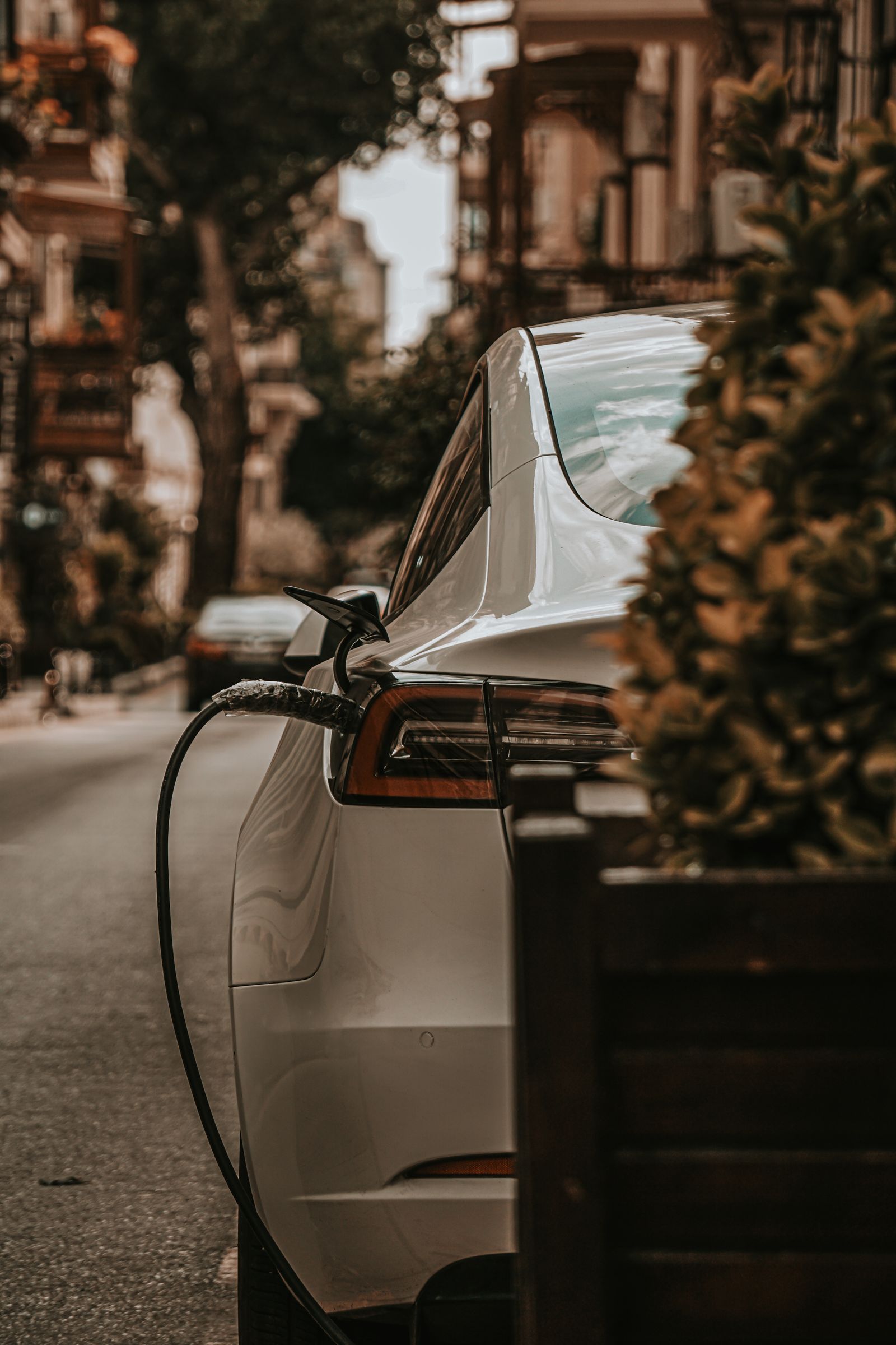 White electric car plugged into a public charger on an urban street