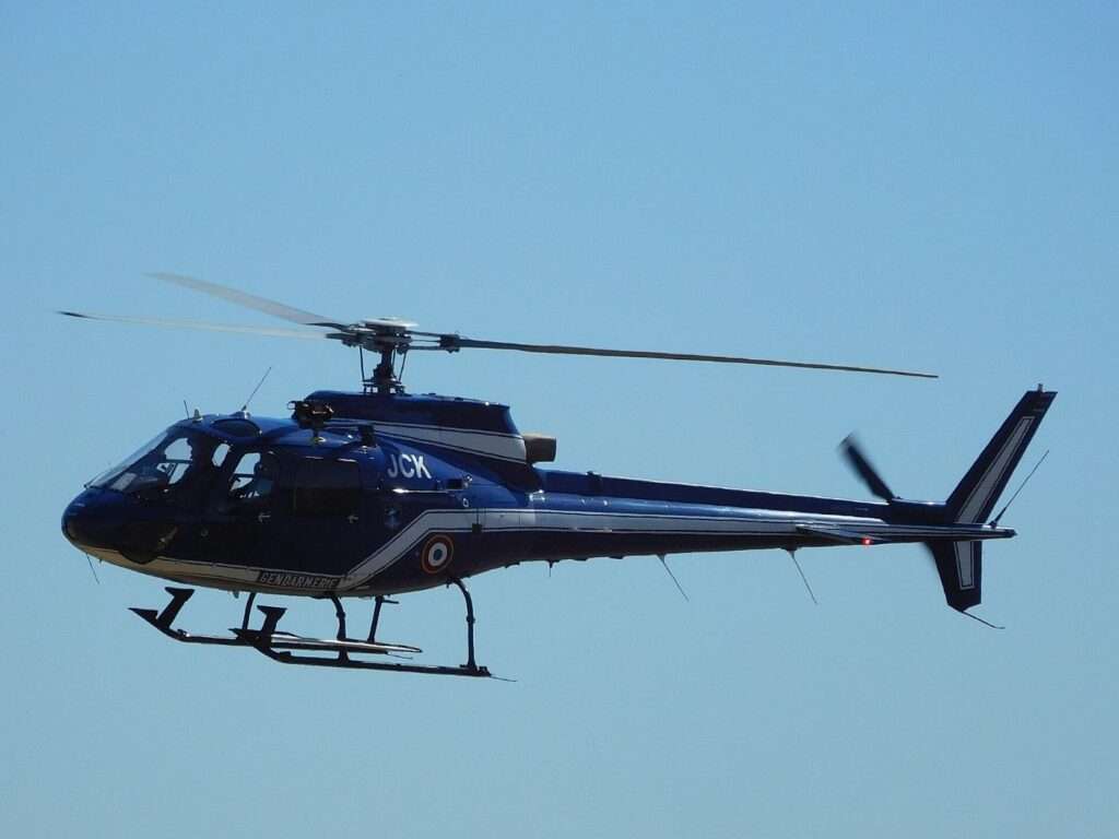 A dark blue Eurocopter AS350 helicopter in flight against a blue sky