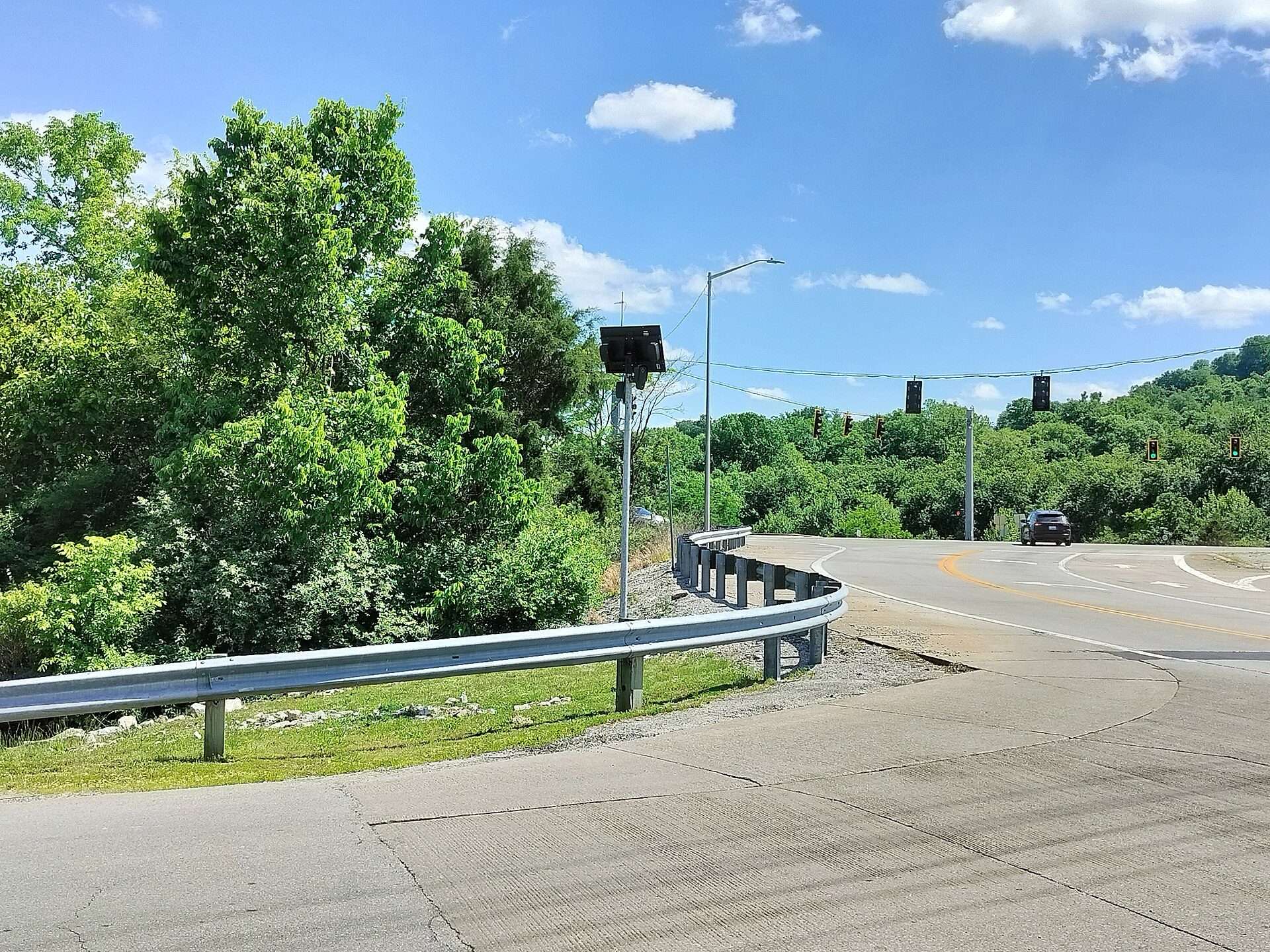 A Flock license plate reader camera on a pole beside a curving road and guardrail in Frankfort, Kentucky