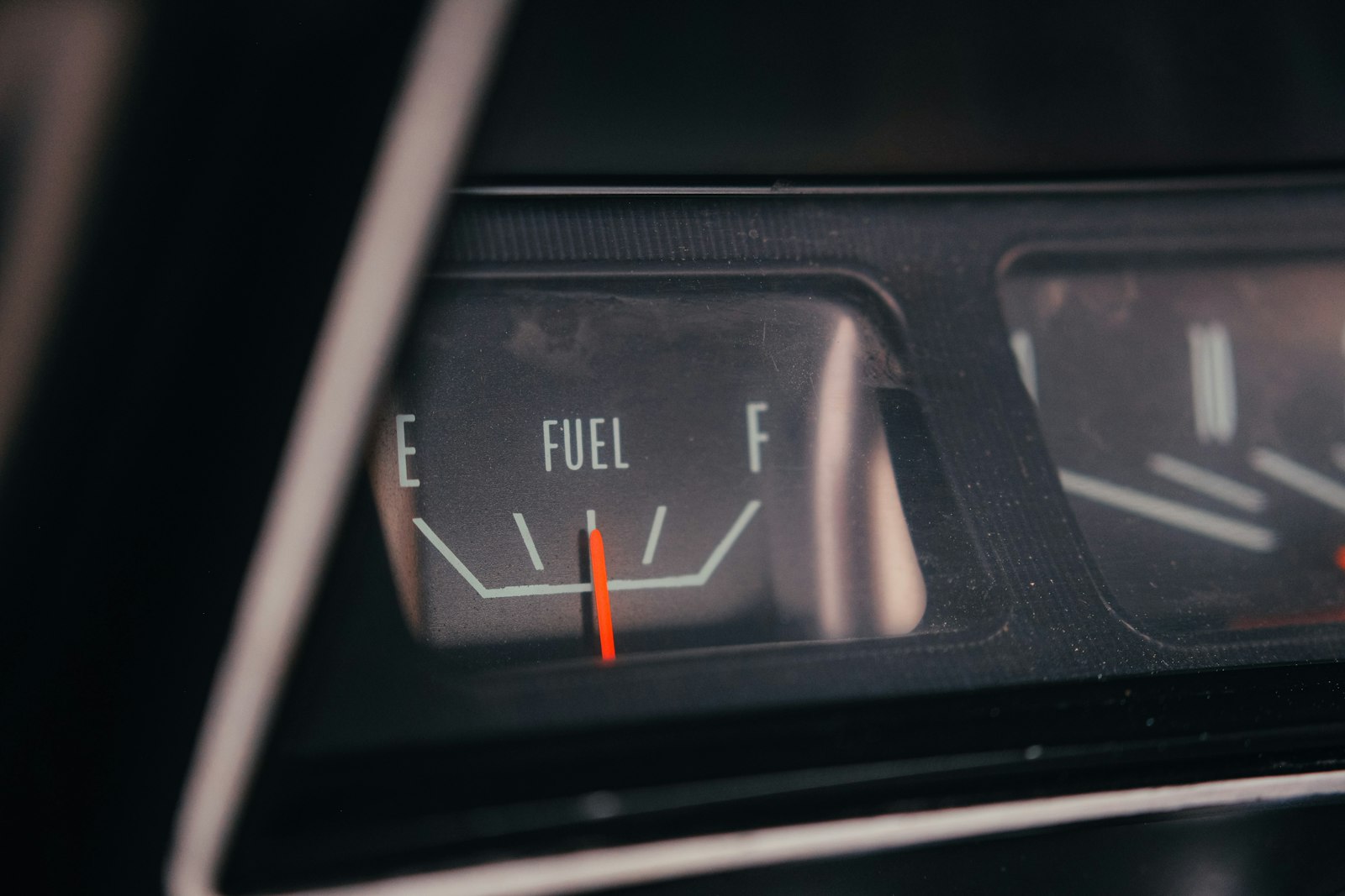 Close-up of a car fuel gauge reading empty with the low-fuel warning light illuminated
