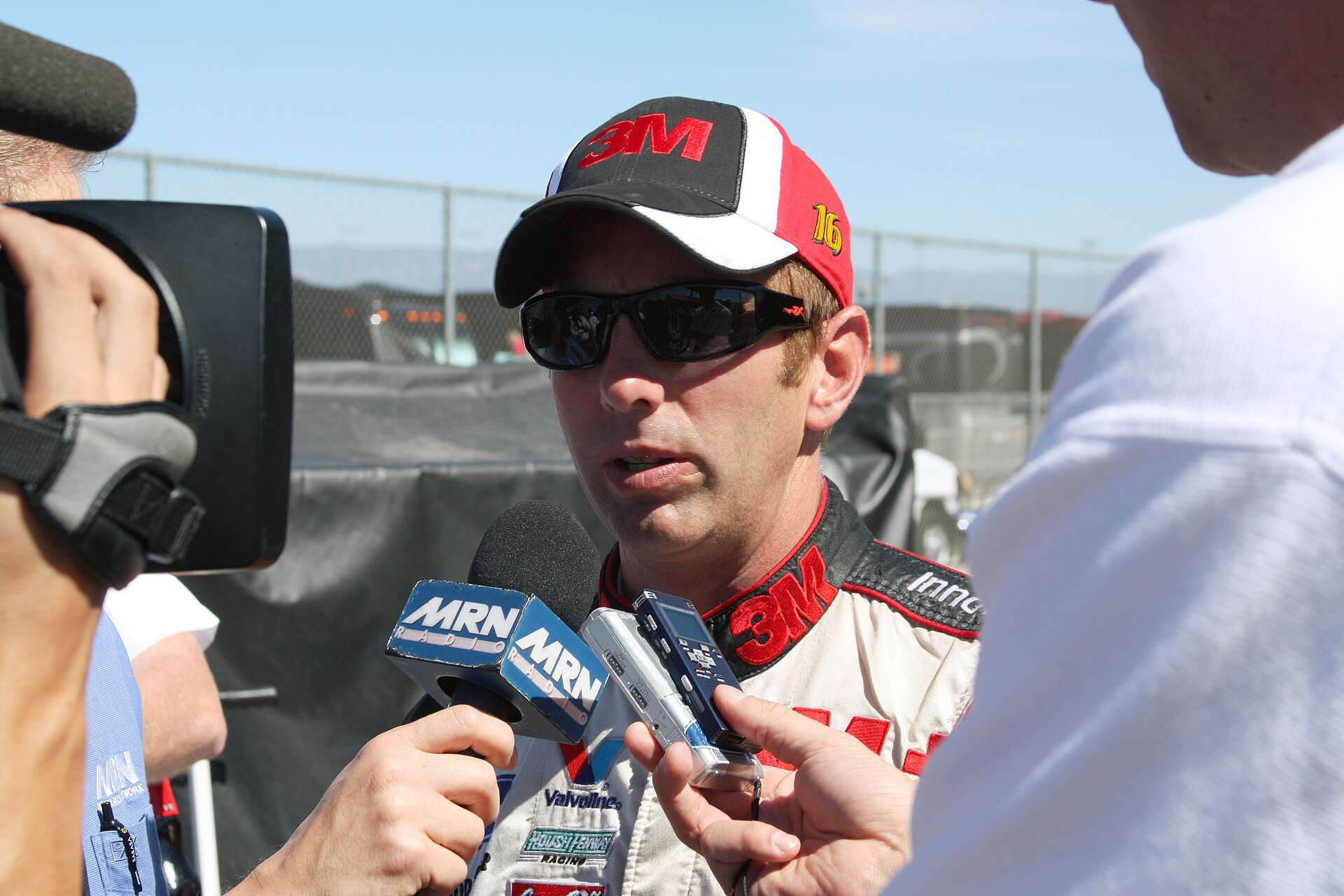 Former NASCAR driver Greg Biffle in a 3M cap speaking into reporters’ microphones