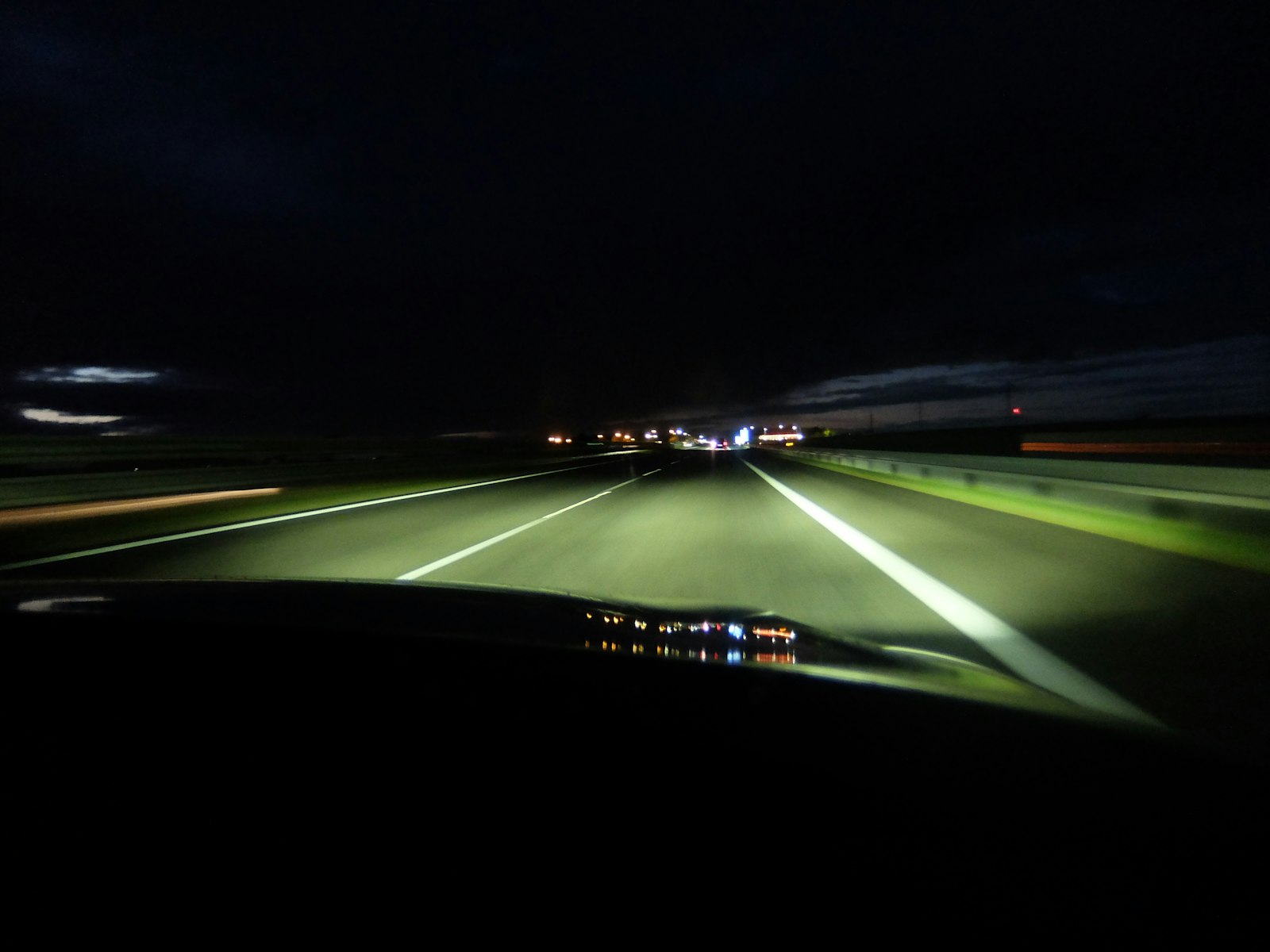 View through a windshield of a multi-lane highway at night lit only by headlights