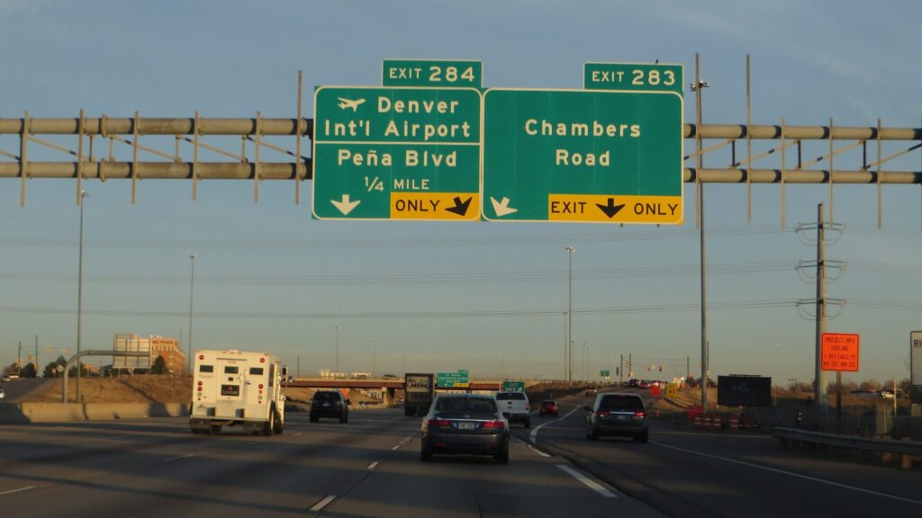 Cars and a truck on Interstate 70 in Denver, Colorado, under exit signs for Denver International Airport and Chambers Road
