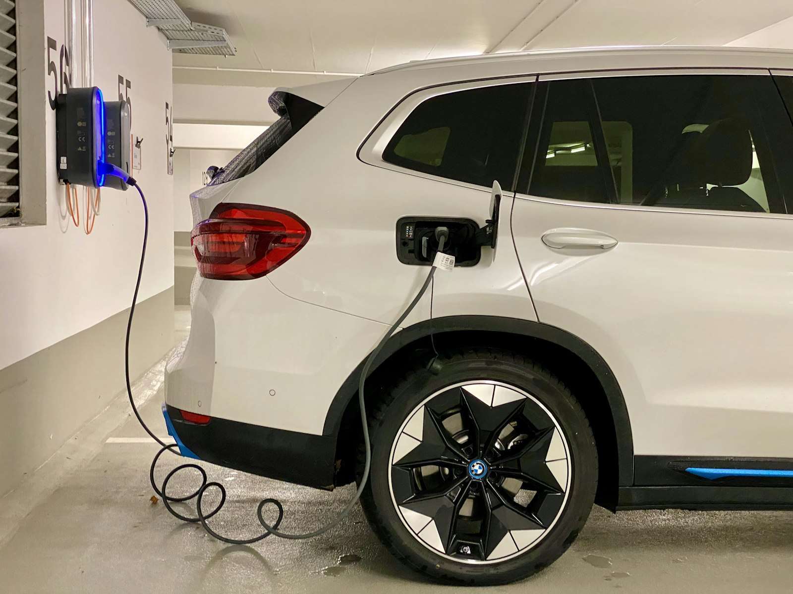 White electric SUV plugged into a wall charger in a parking garage