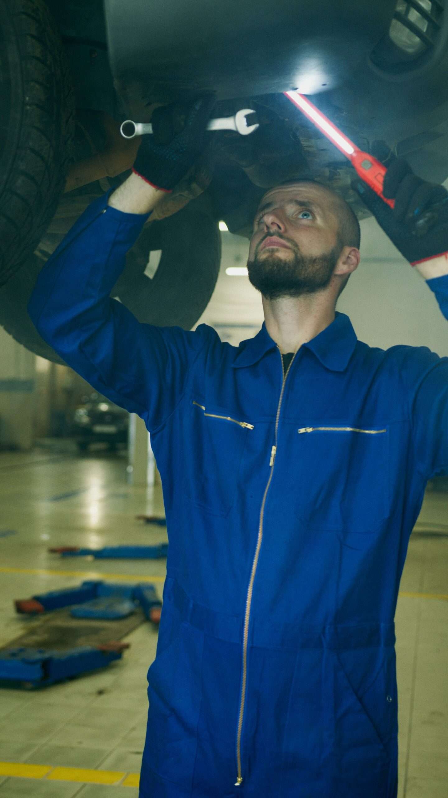 Technician working underneath a vehicle with a hand light during a repair