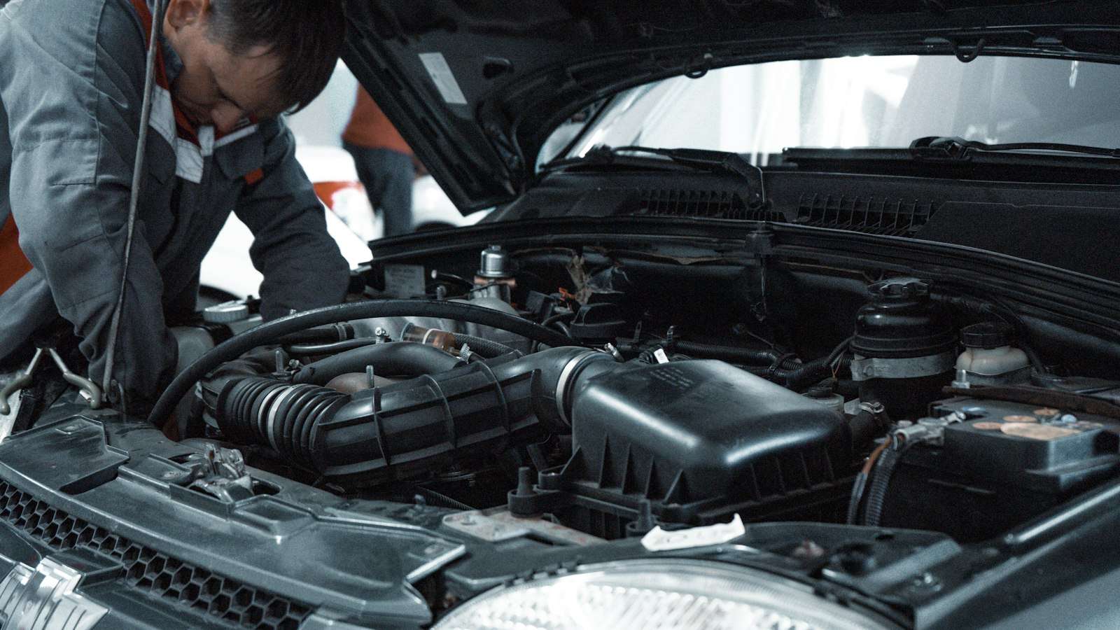 A mechanic in a grey uniform inspecting a car engine