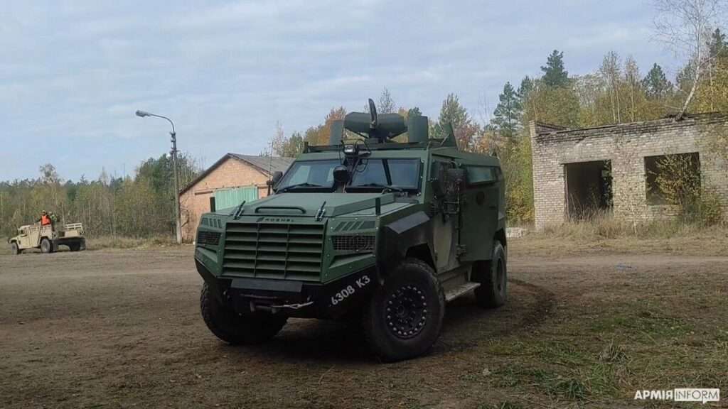A green Roshel Senator armoured vehicle parked on a dirt lot