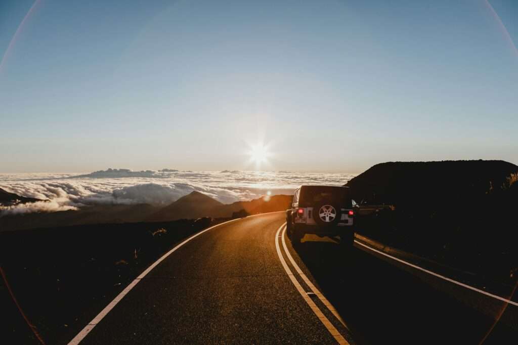 An SUV drives along a winding mountain road at sunrise on a weekend road trip