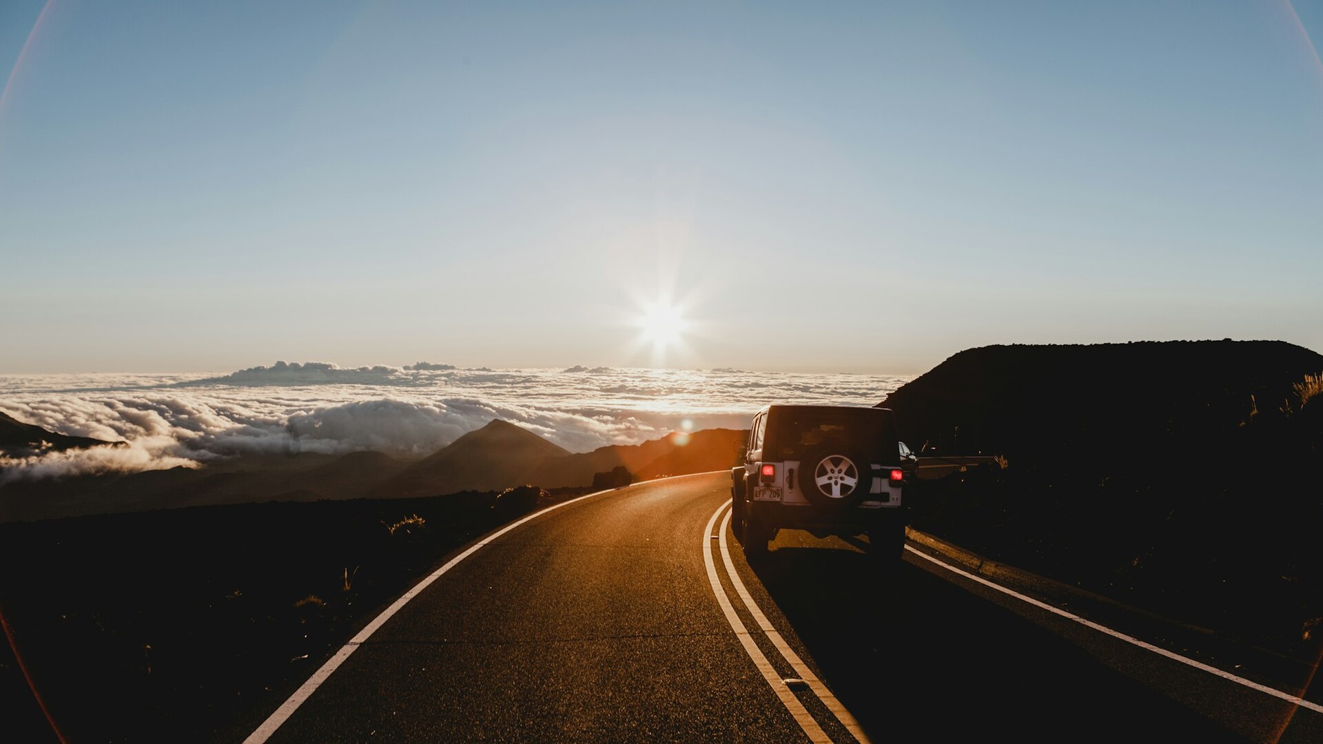 An SUV drives along a winding mountain road at sunrise on a weekend road trip
