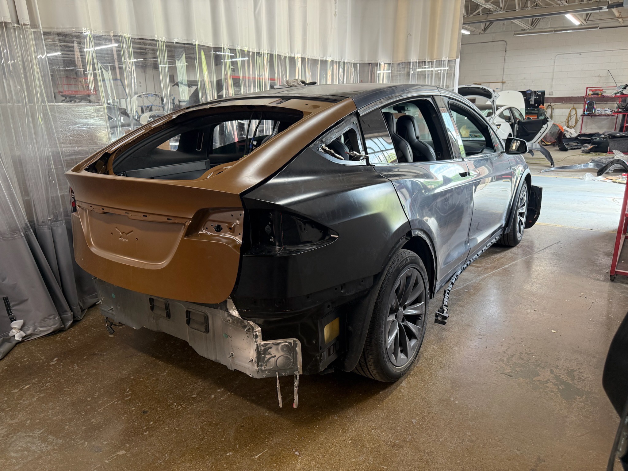 A Tesla with rear-end collision damage undergoing repair in a body shop