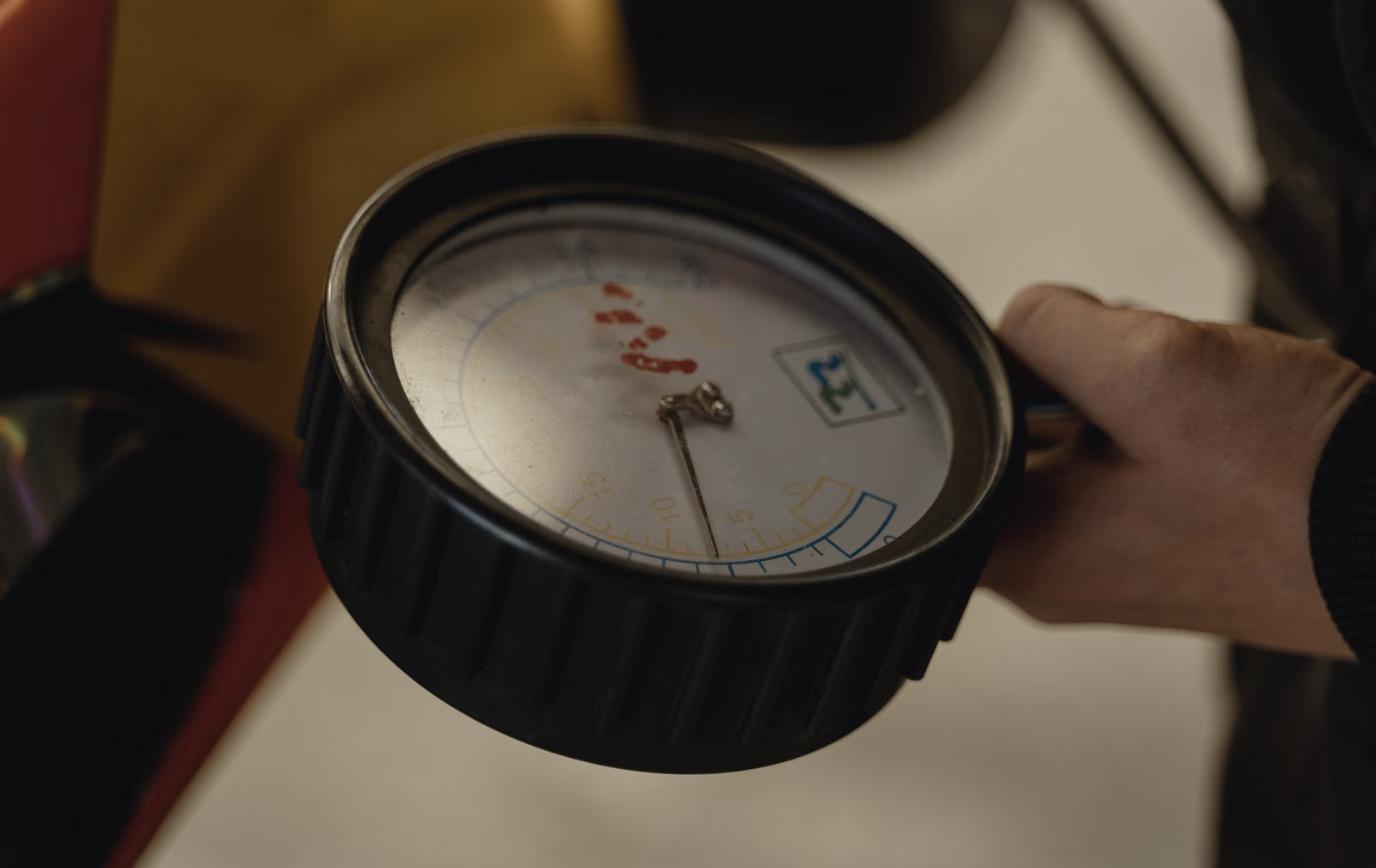Hand holding an analog tire pressure gauge against a wheel