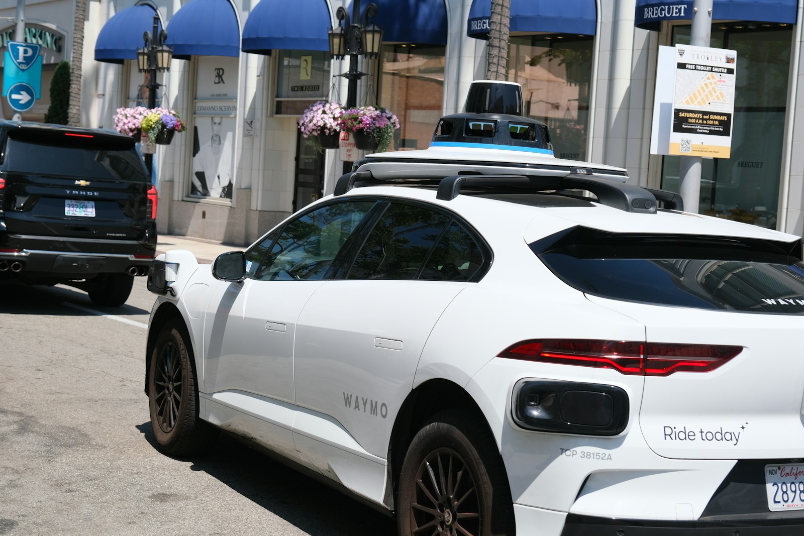 A white Waymo autonomous vehicle with roof sensors parked on a city street