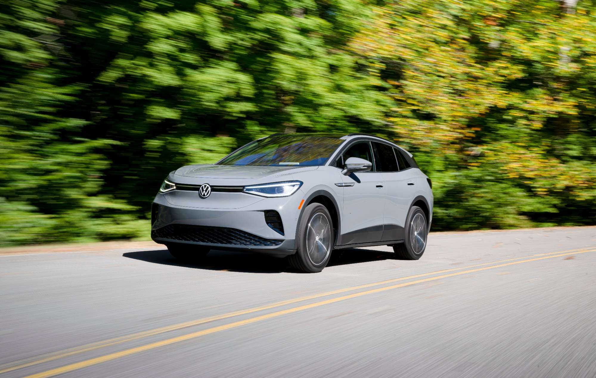 A silver 2023 Volkswagen ID.4 driving on a two-lane road past trees