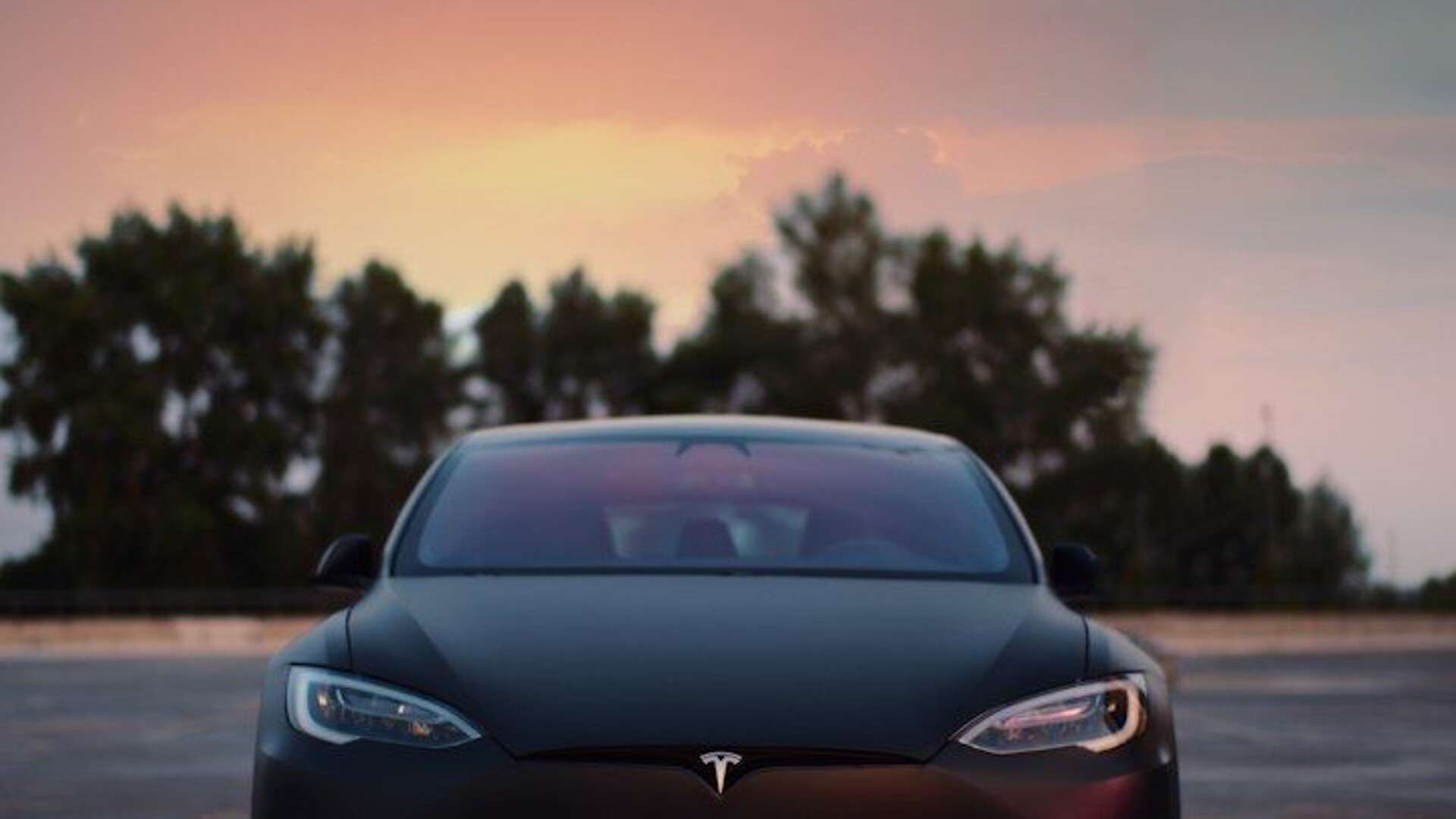 A matte black electric car parked on a concrete lot under a warm sky