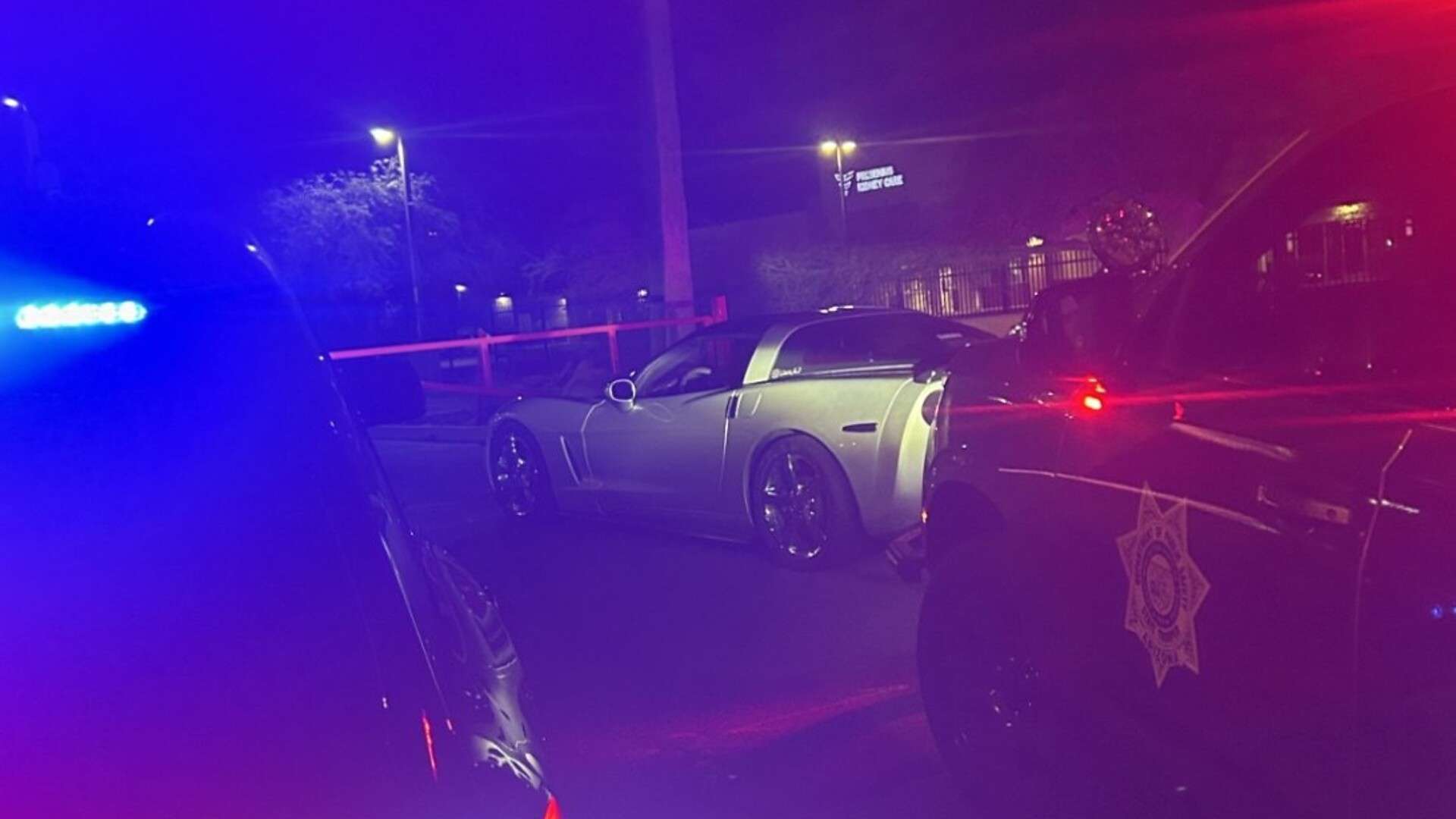 Silver Chevrolet Corvette stopped at night between two Arizona DPS Highway Patrol vehicles with emergency lights on, after a racing arrest on I-10 in Phoenix