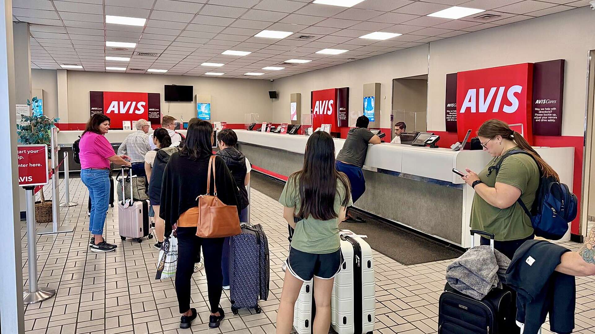 Customers wait in line at an Avis car rental counter at Philadelphia International Airport