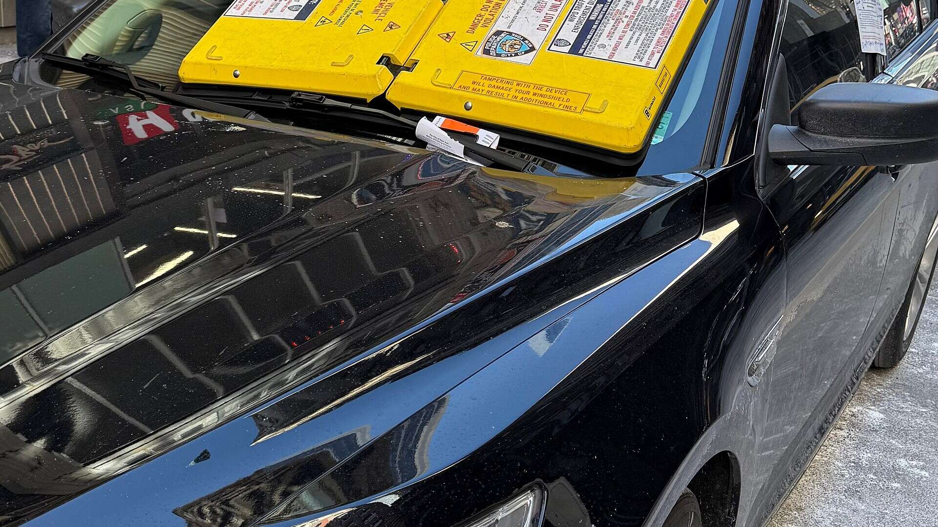 A yellow Barnacle parking immobilization device suction-mounted across a car windshield