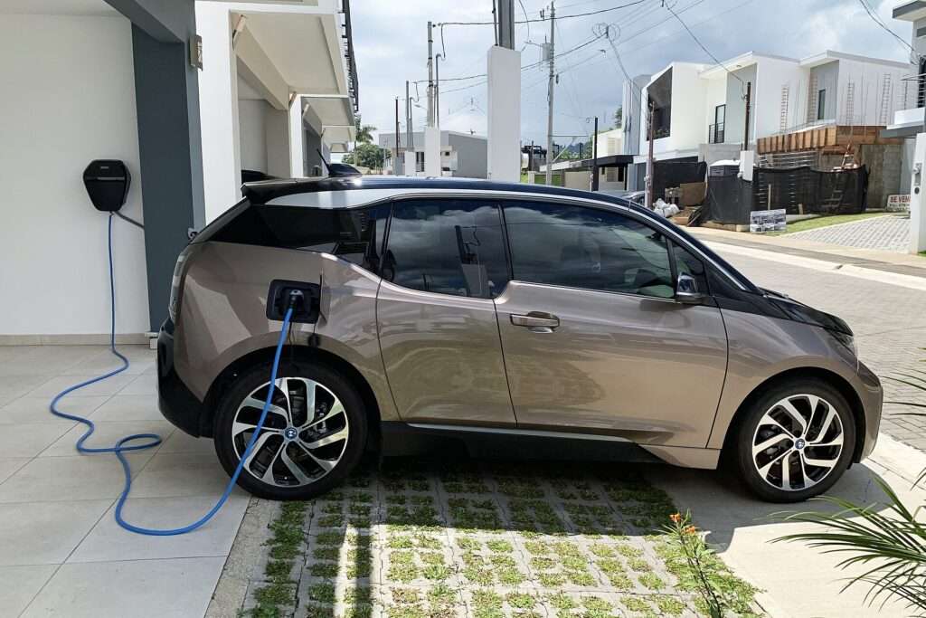 A BMW i3 plugged into a Level 2 wall charger in a residential driveway