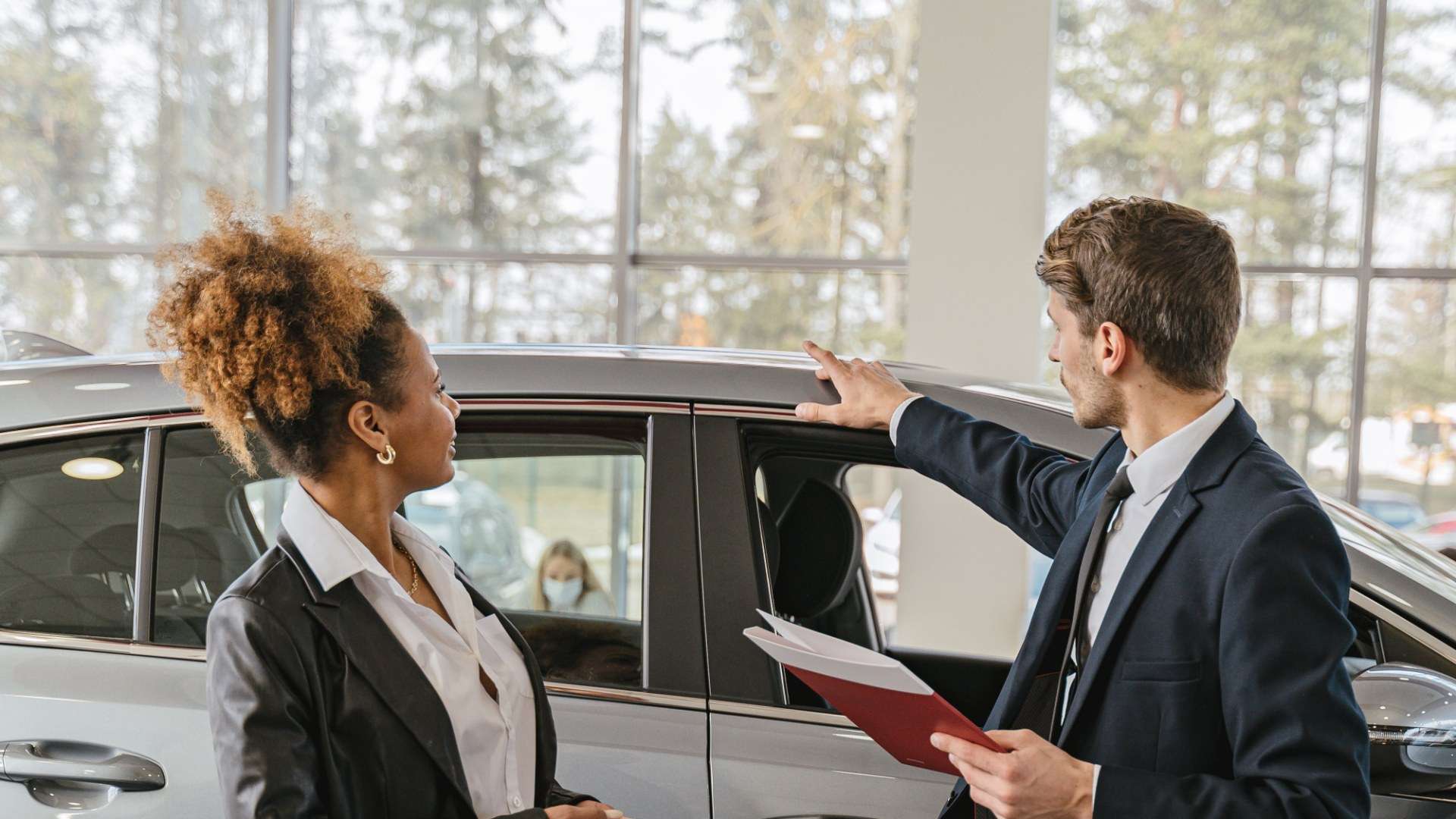 A car salesman talks with a customer about vehicle options inside a dealership showroom