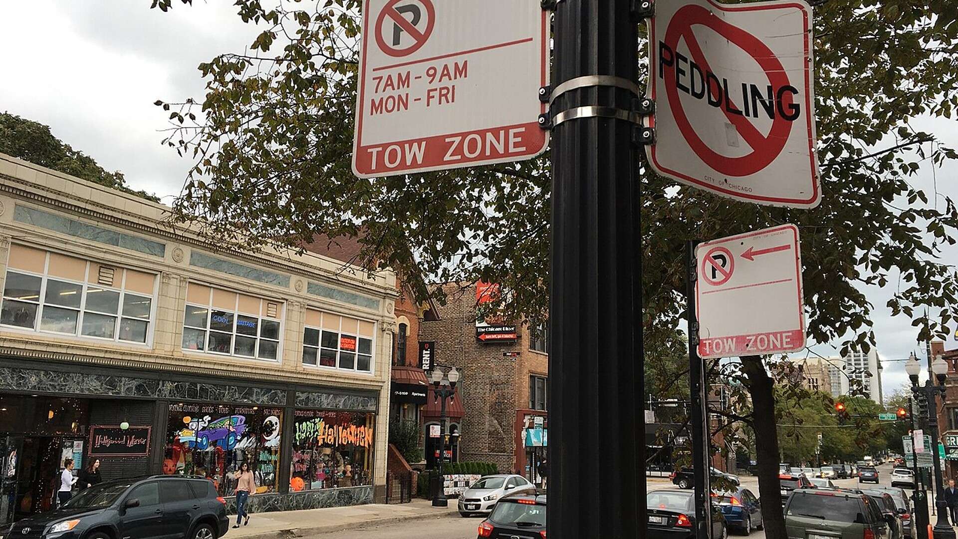 Red-and-white Tow Zone and No Peddling signs on a pole above parked cars on a Chicago street