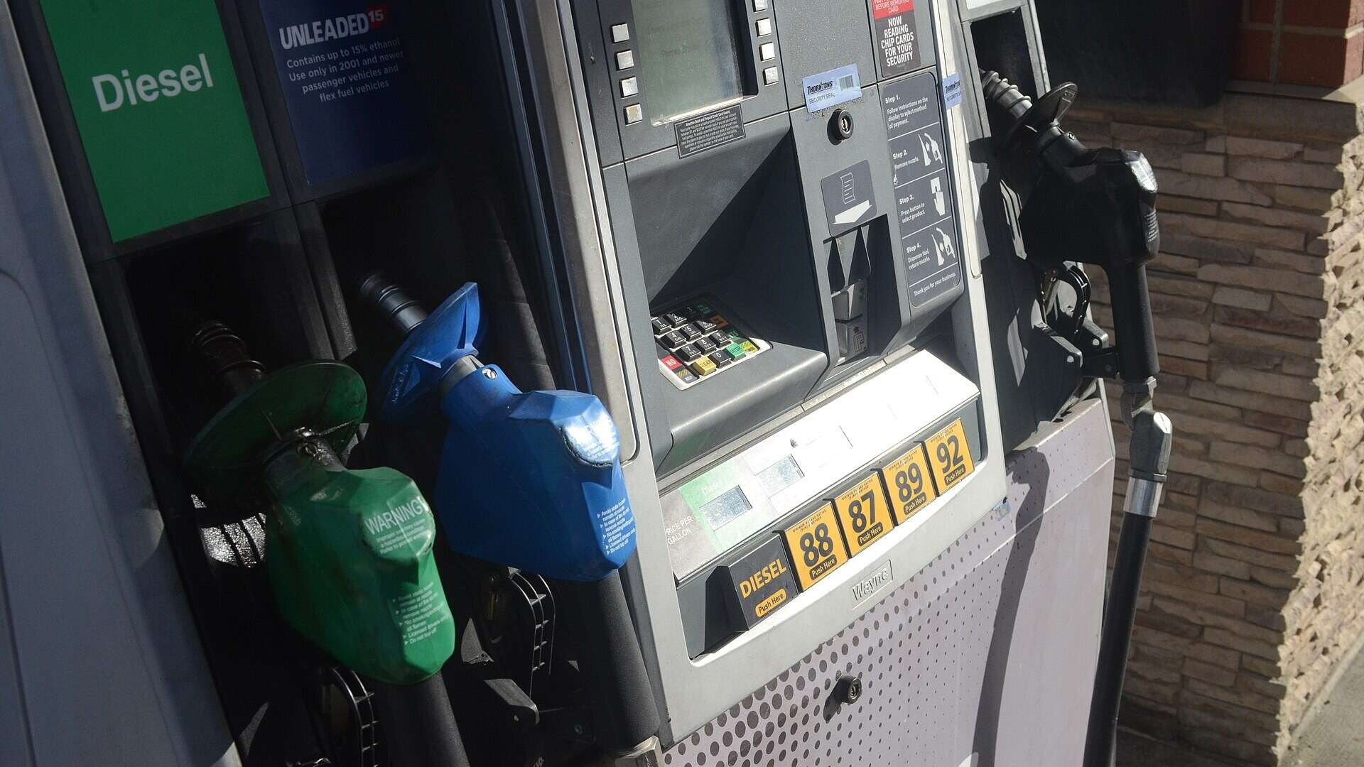 A fuel dispenser with a green diesel nozzle and a blue gasoline nozzle beside a card reader and keypad