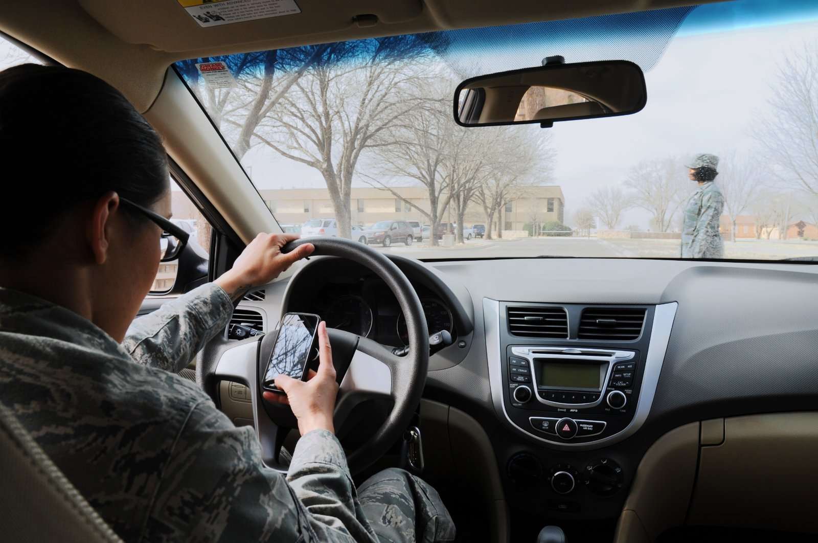 A driver holds a smartphone while gripping the steering wheel