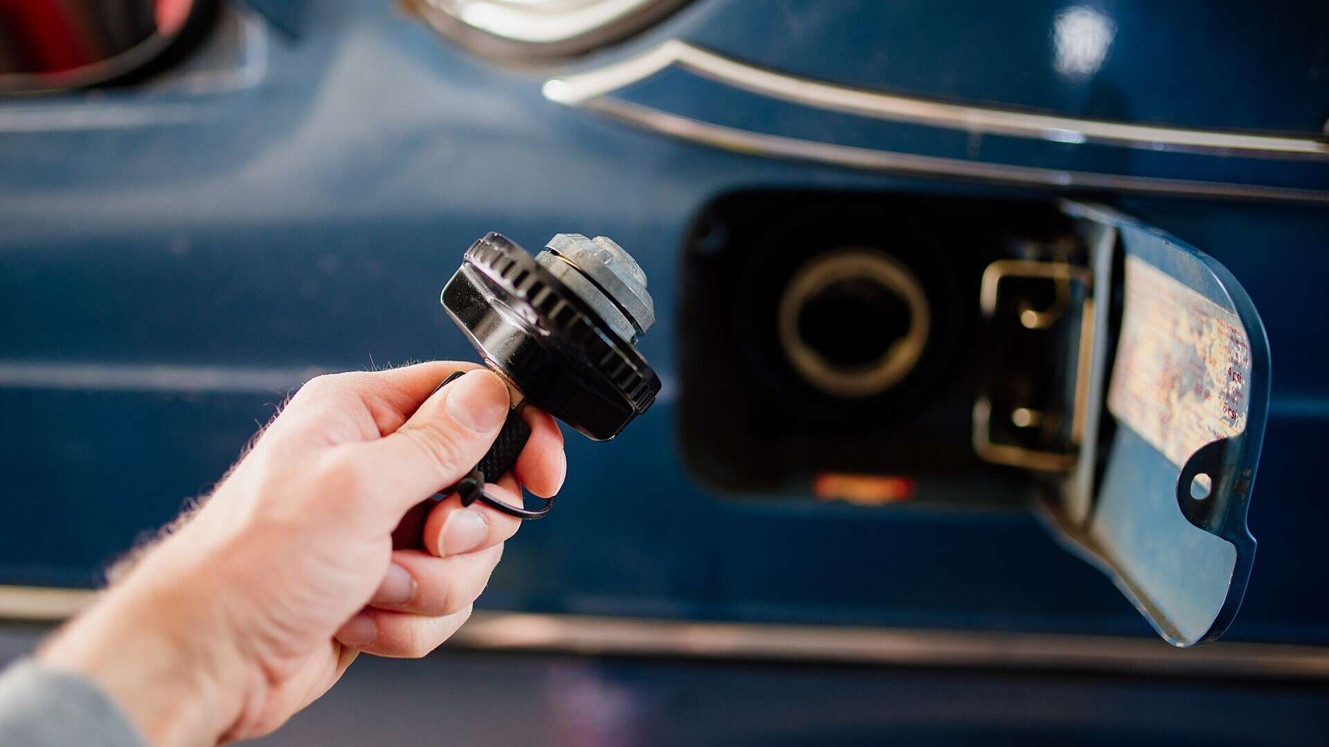 A driver holds a fuel cap while preparing to refuel a car at a gas station