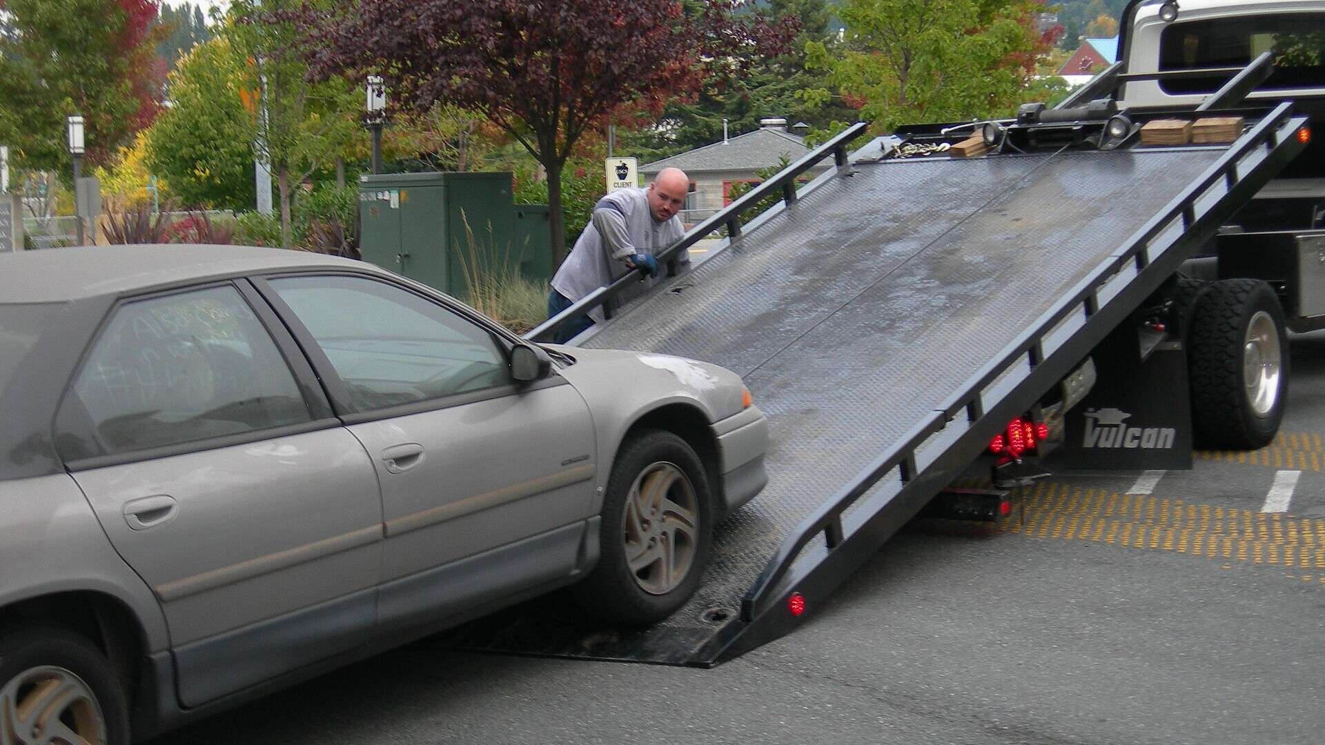 A flatbed tow truck winching a silver sedan onto its bed