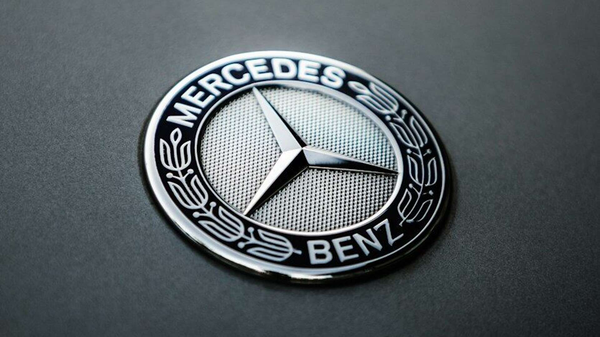 A circular Mercedes-Benz emblem with a three-pointed star on a dark matte surface