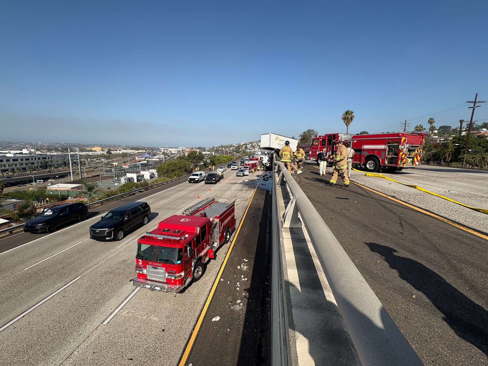Fire engines and firefighters on both levels of a split I-5 near Washington Street in San Diego, with the wrecked moving truck visible in the distance.