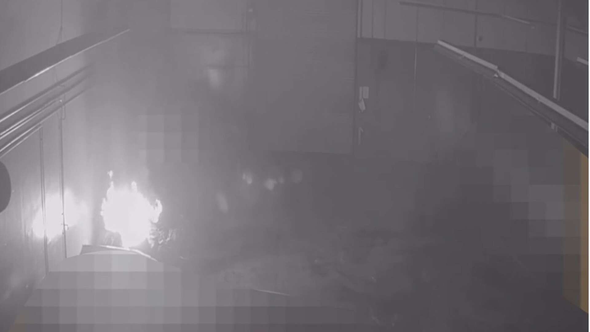Grainy black-and-white surveillance frame timestamped 11:43 p.m. Oct. 14, 2026, showing flames and spreading smoke on the left side of a storage area, with unrelated vehicles pixelated