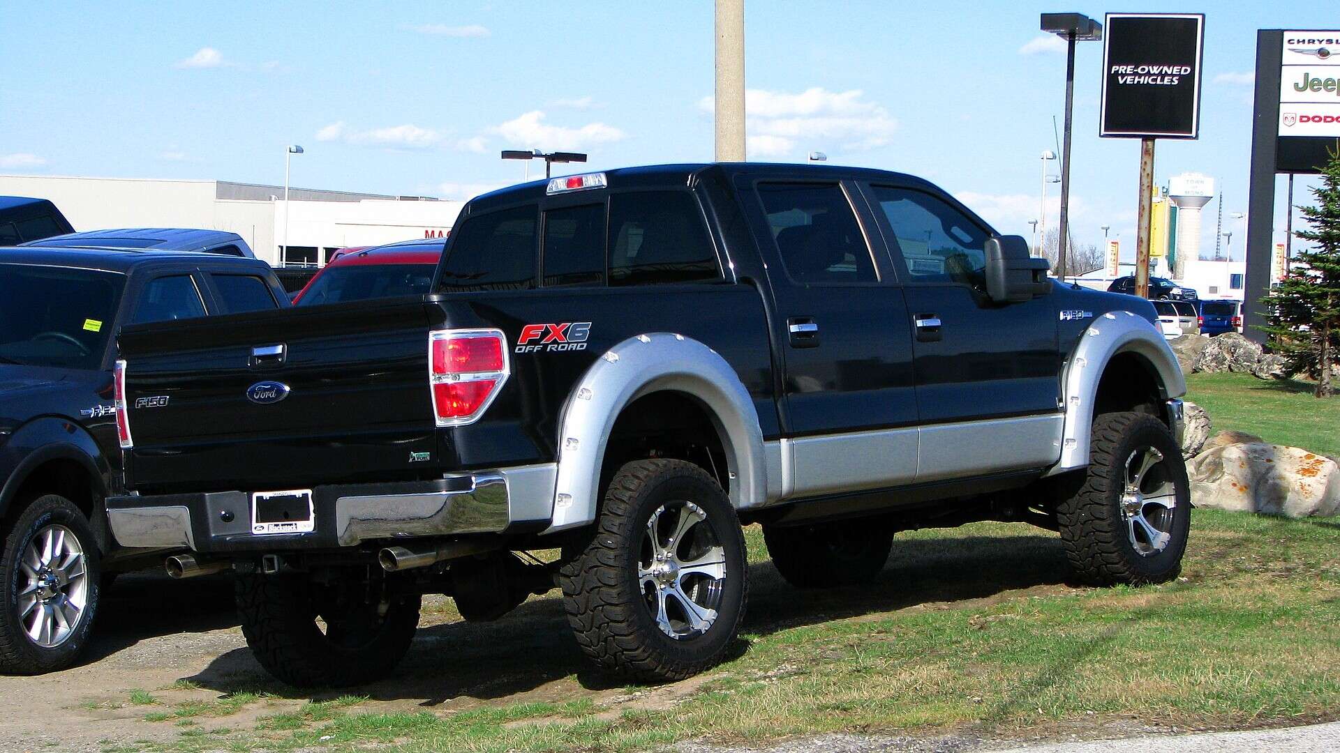 A lifted Ford F-150 with oversized tires parked on a dealership lot