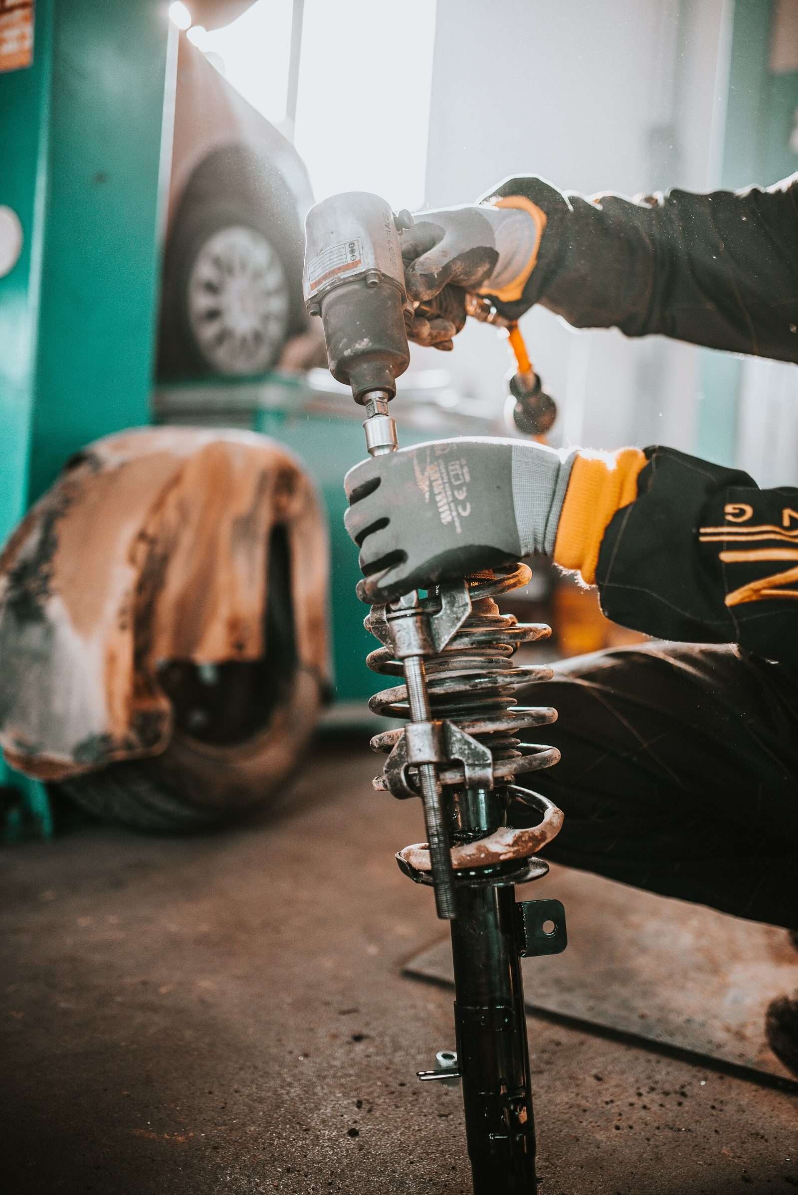 A mechanic uses an impact wrench on a coil-spring strut assembly in a repair shop