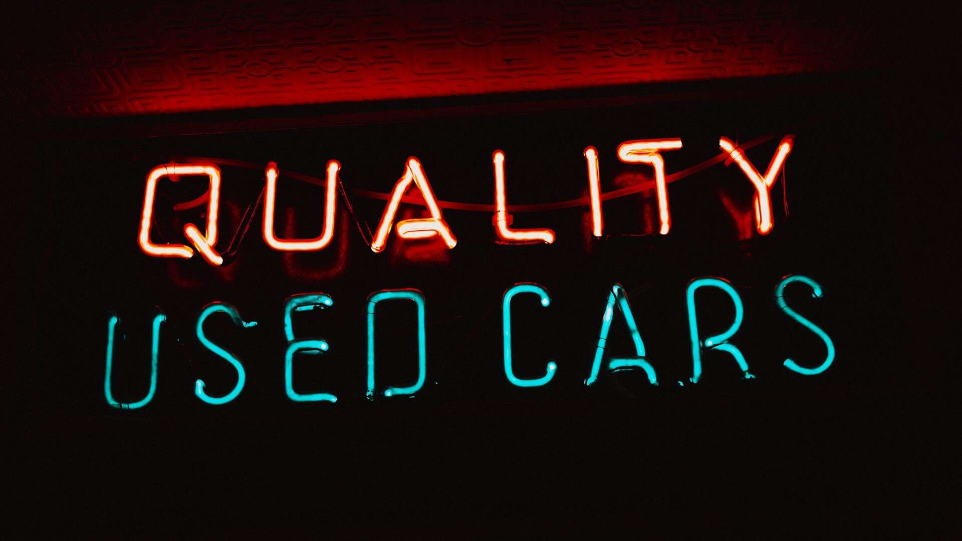 Red and blue neon sign reading Quality Used Cars against a dark wall