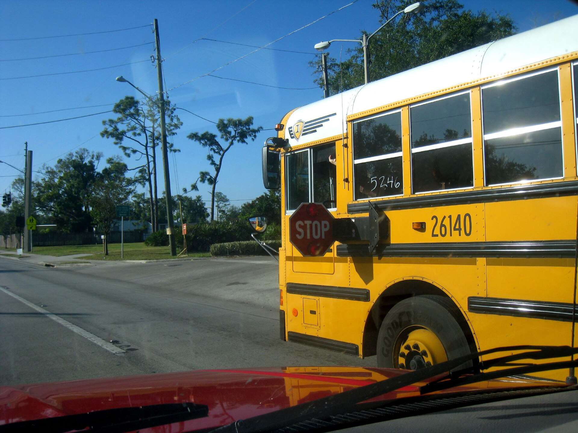A yellow school bus with its red stop arm extended, seen from a car stopped behind it