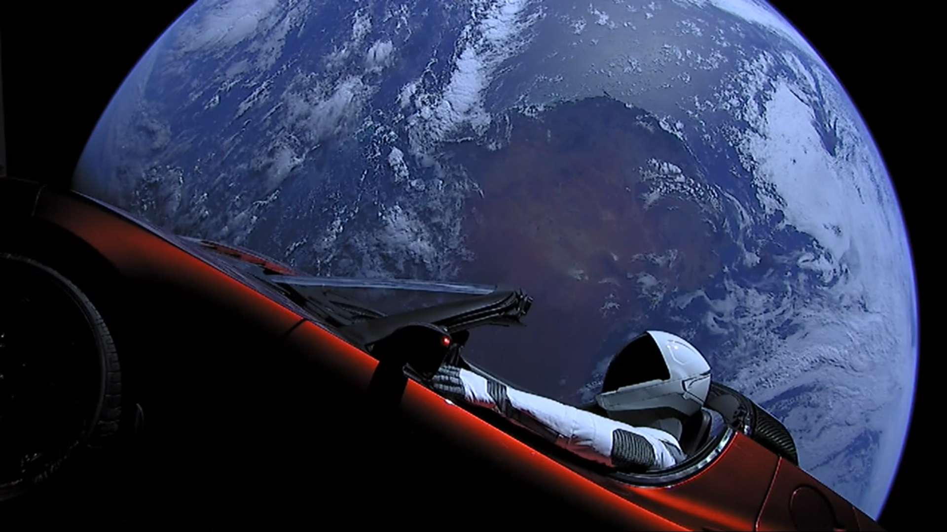 A Tesla Roadster with a spacesuited mannequin in the driver seat, with Earth in the background