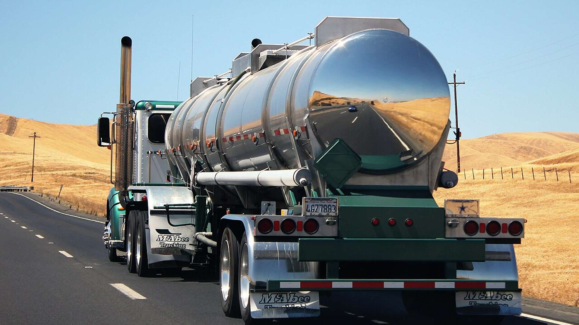 A chrome tanker semitruck traveling on Interstate 5 through dry hills in Fresno County, California
