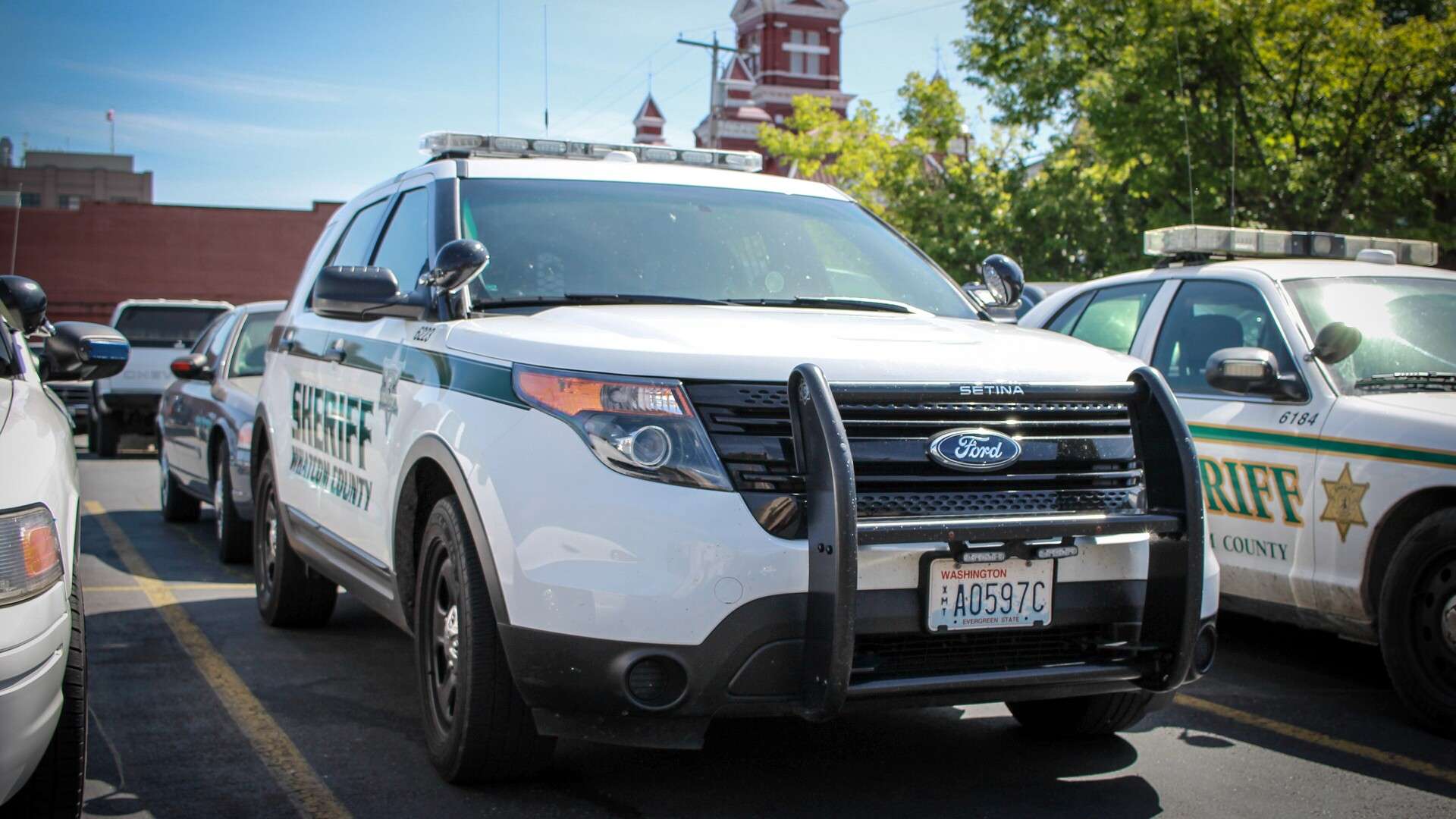 A white Whatcom County Sheriff Ford Police Interceptor Utility with a push bumper parked in a lot beside other patrol vehicles